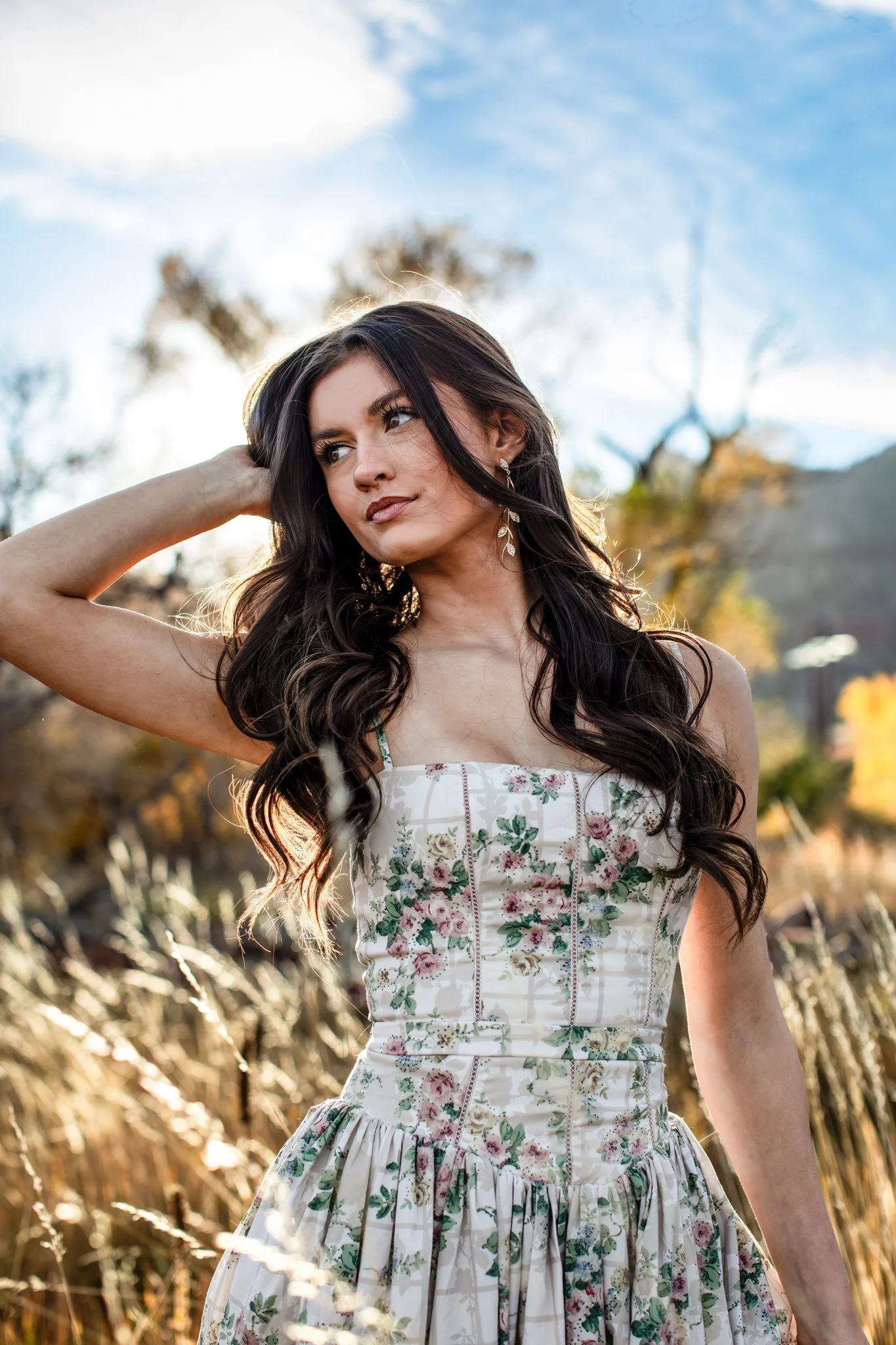 Artistic sunset portrait of a high school senior girl with the sunset behind her wearing a floral dress.