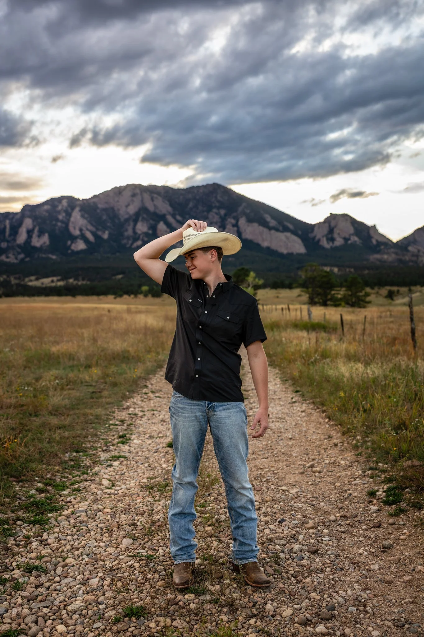 Erie Colorado High School Photographer takes portrait of Erie Colorado High School Senior standing in jeans and holding onto his cowboy hat with the backdrop of the flatiron mountians.