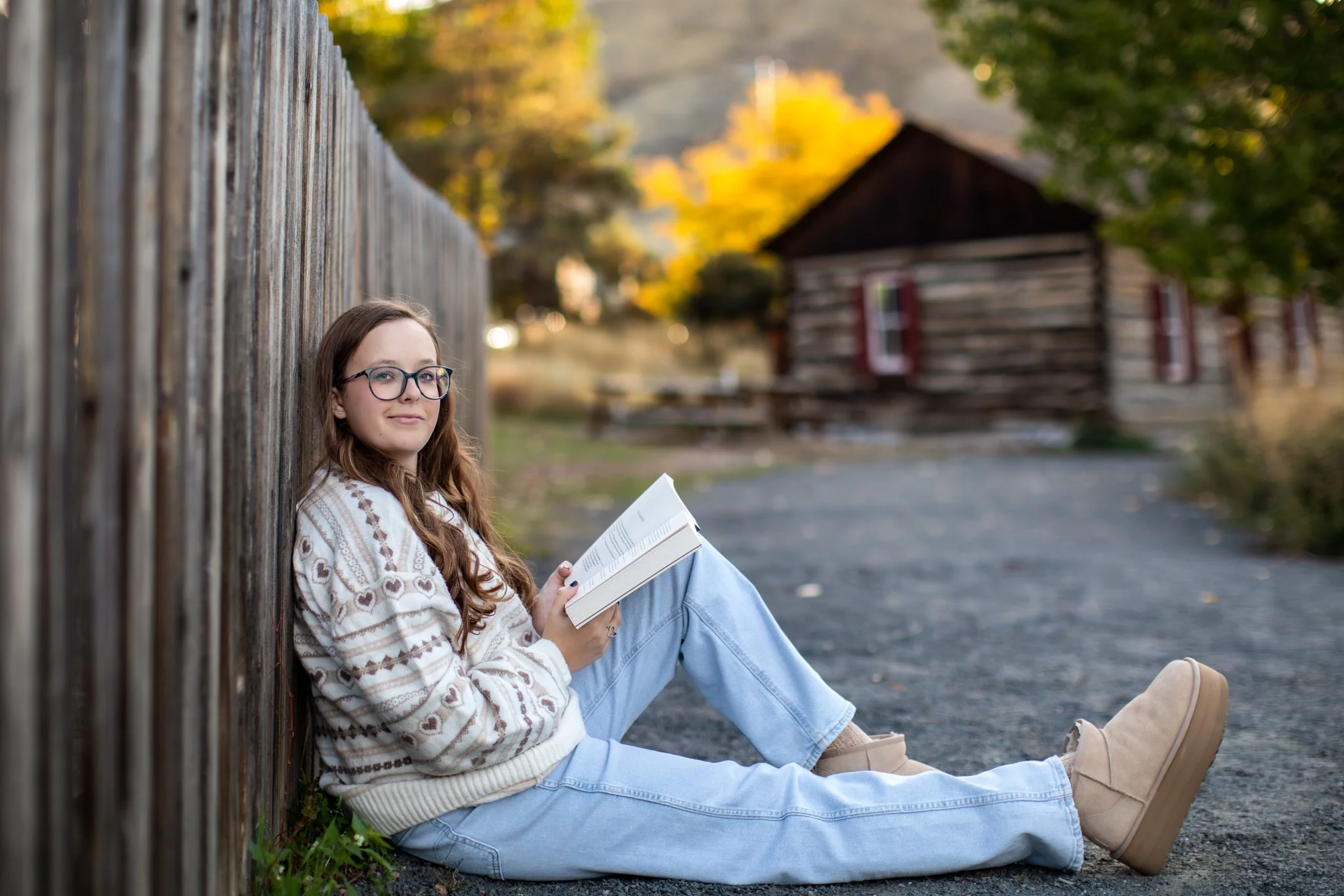 Golden Colorado High School Senior Photographer takes a picture of a high school senior girl sitting against a fence in a park reading a book.