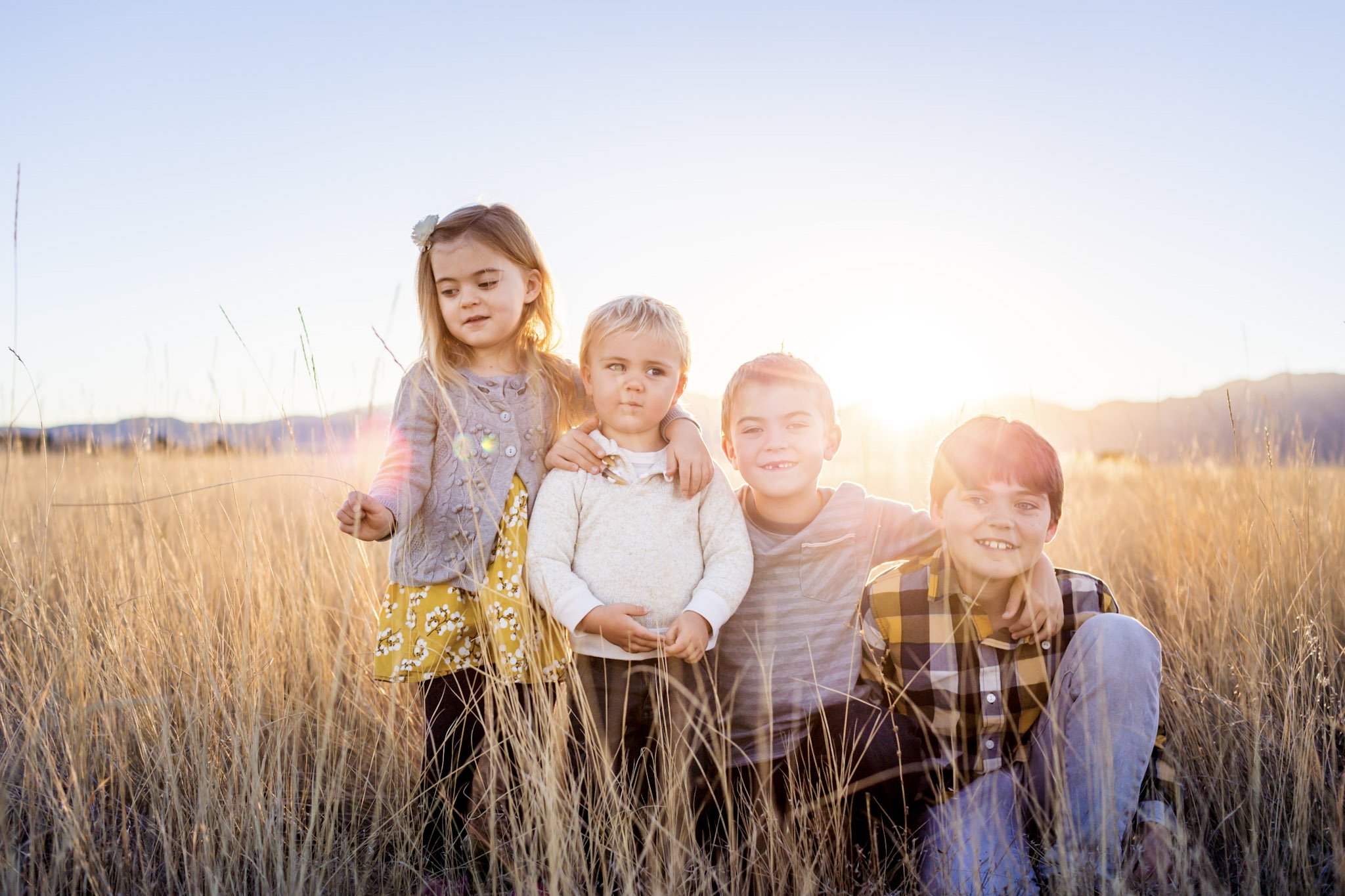 Four children standing in a field at sunset, with mountains in the background, enjoying the outdoors.