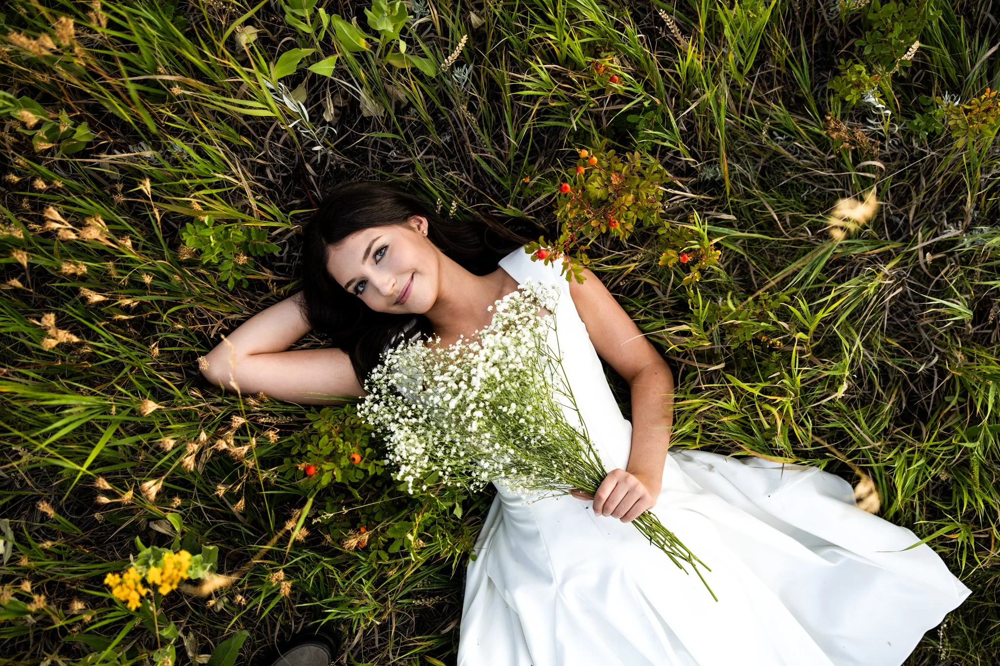 Colorado Photographer captures picture of high school senior laying in a grass surrounded by flowers and holding a bouquet of babies breath.