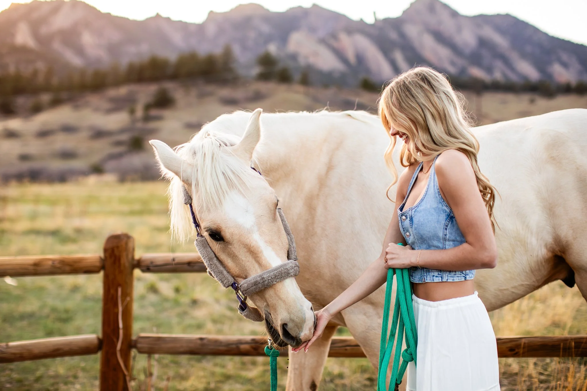 Boulder Colorado High School Senior Photography portrait of a girl in a denim vest, white skirt feeding a white horse.