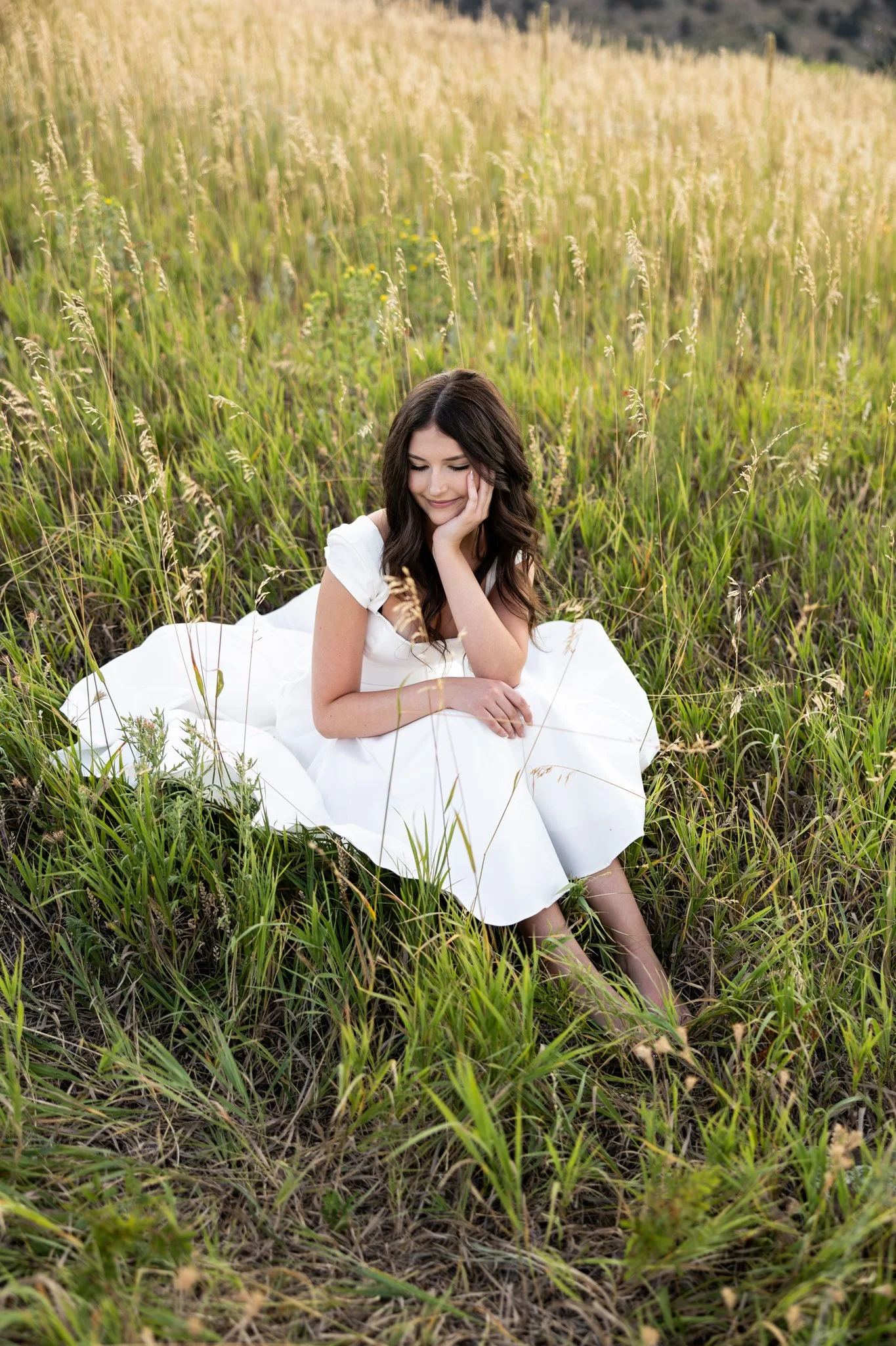 Boulder Colorado High School Senior Photographer captures image of girl in white dress sitting in a the grass bare foot.