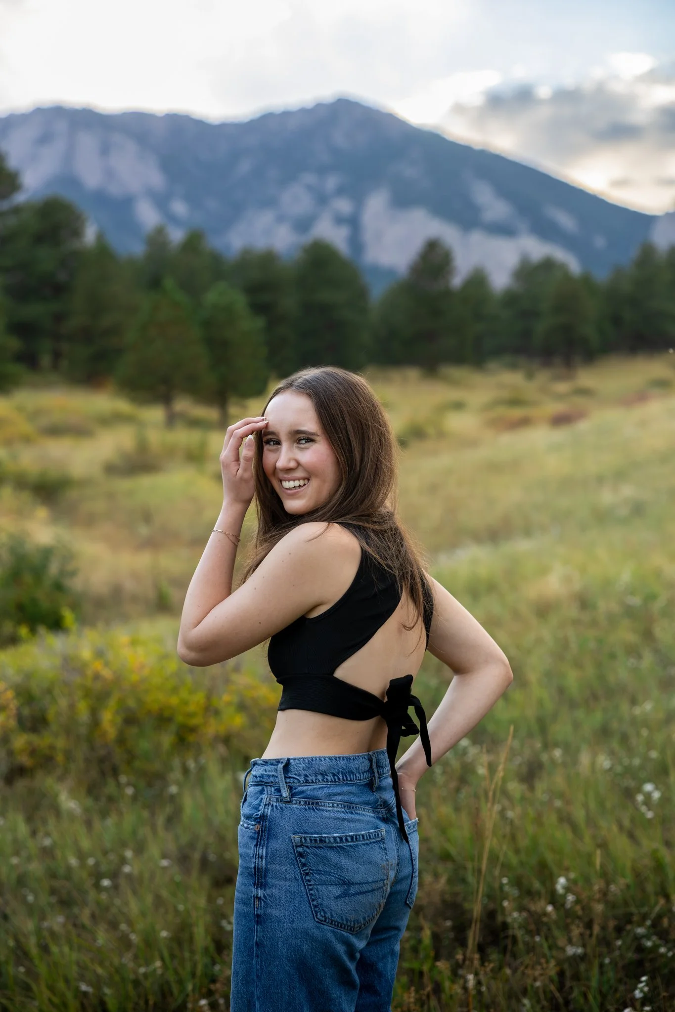 Photograph of a high school senior girl standing in a field in Boulder Colorado with the flatiron mountains in the background.