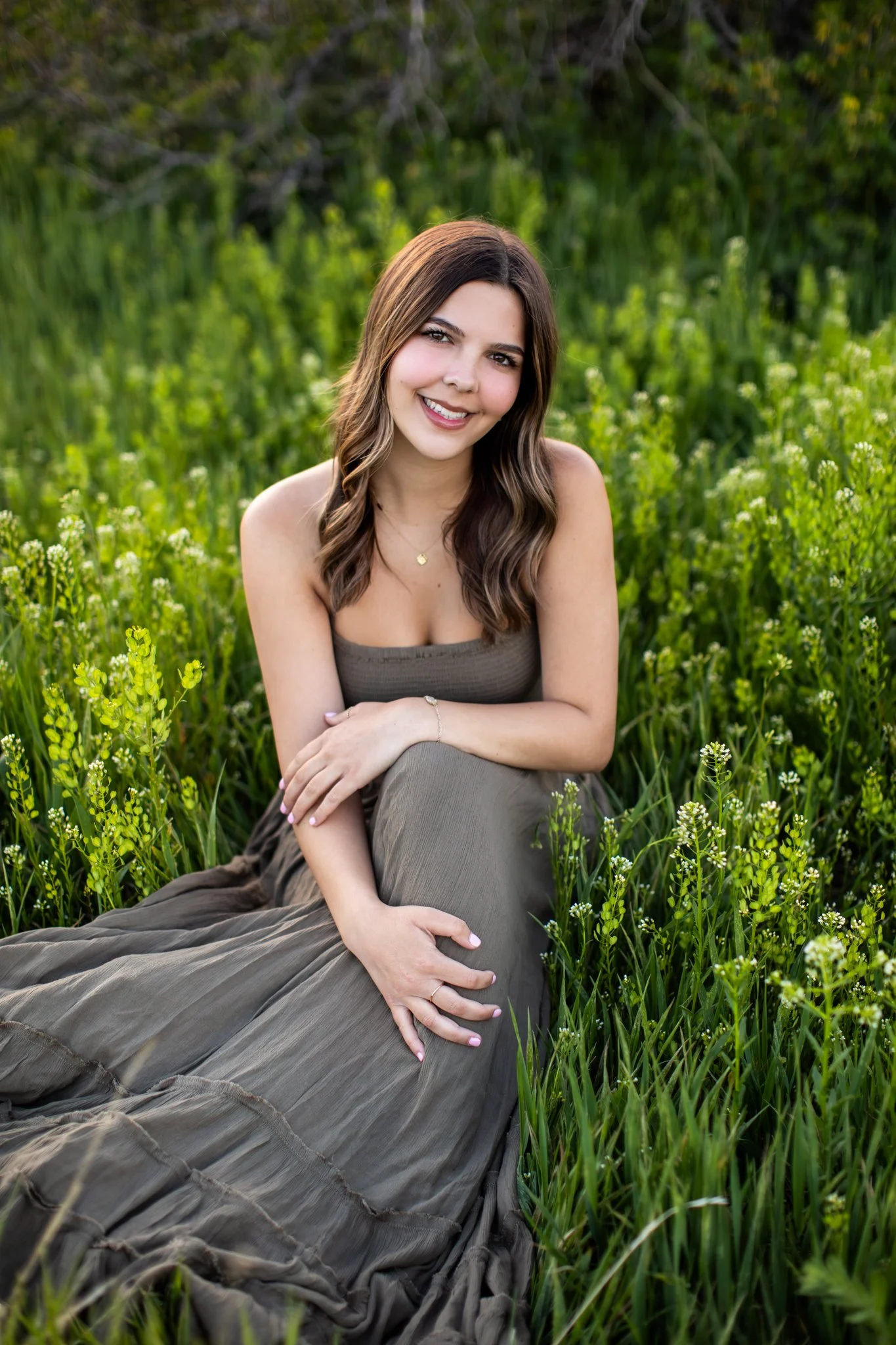 Colorado Senior Photographer captures girl in muted green maxi dress sitting in bright green field.