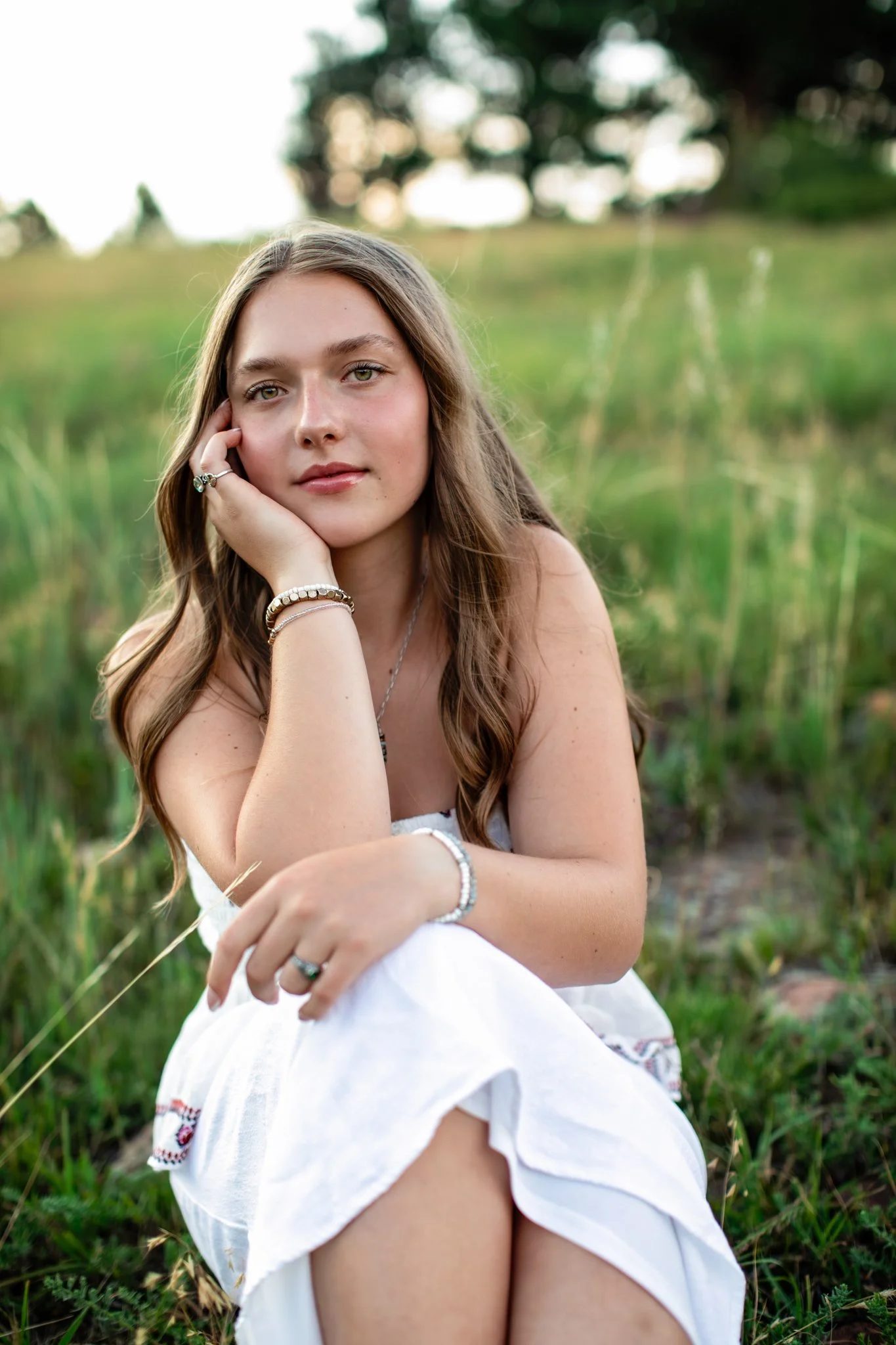 Boulder Colorado Senior Photographer in a white dress sitting in green feild