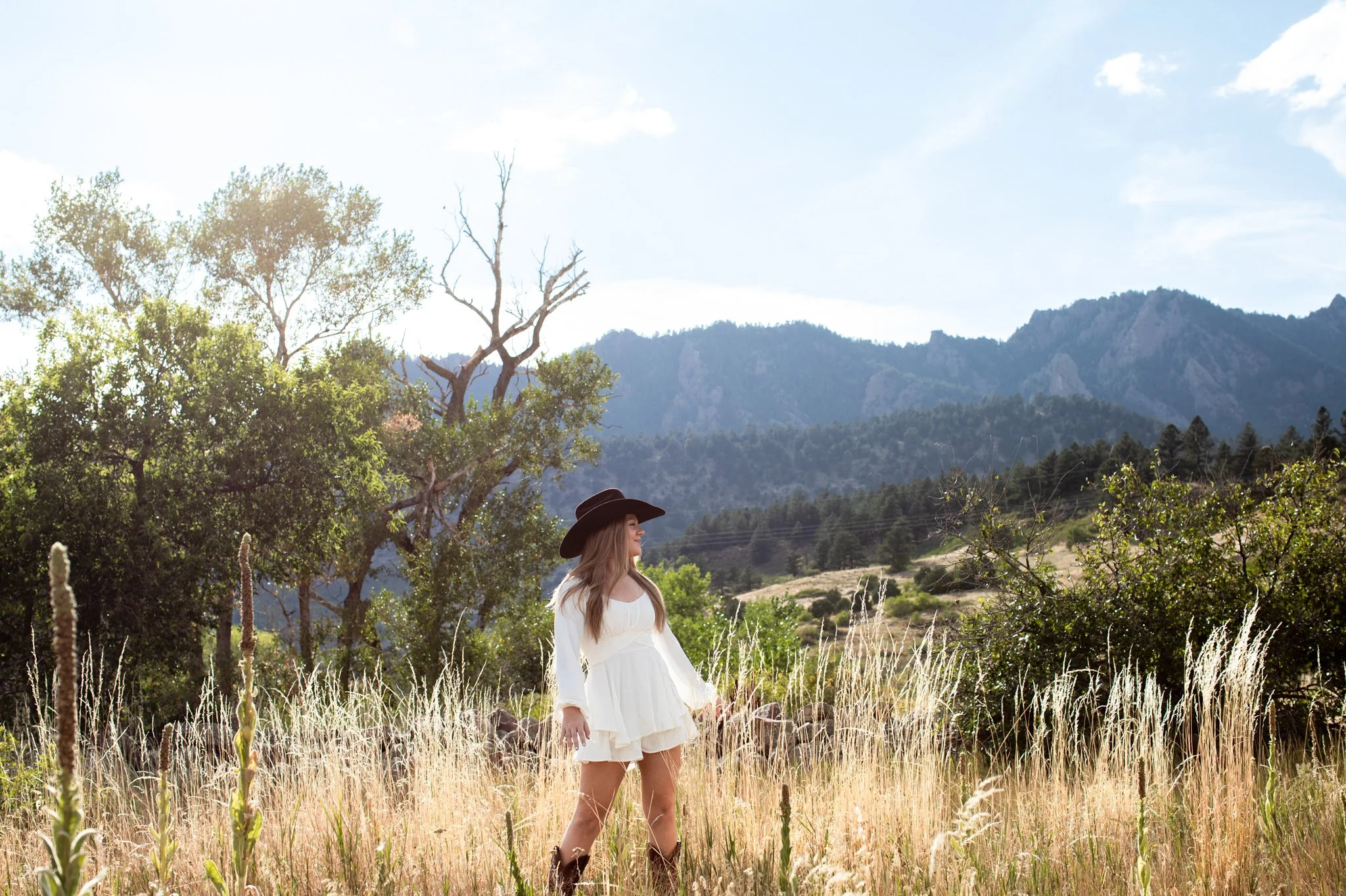 Boulder Senior Photographer captures scenic picture of girl in short white dress, cowboy boots and black cowboy hat.