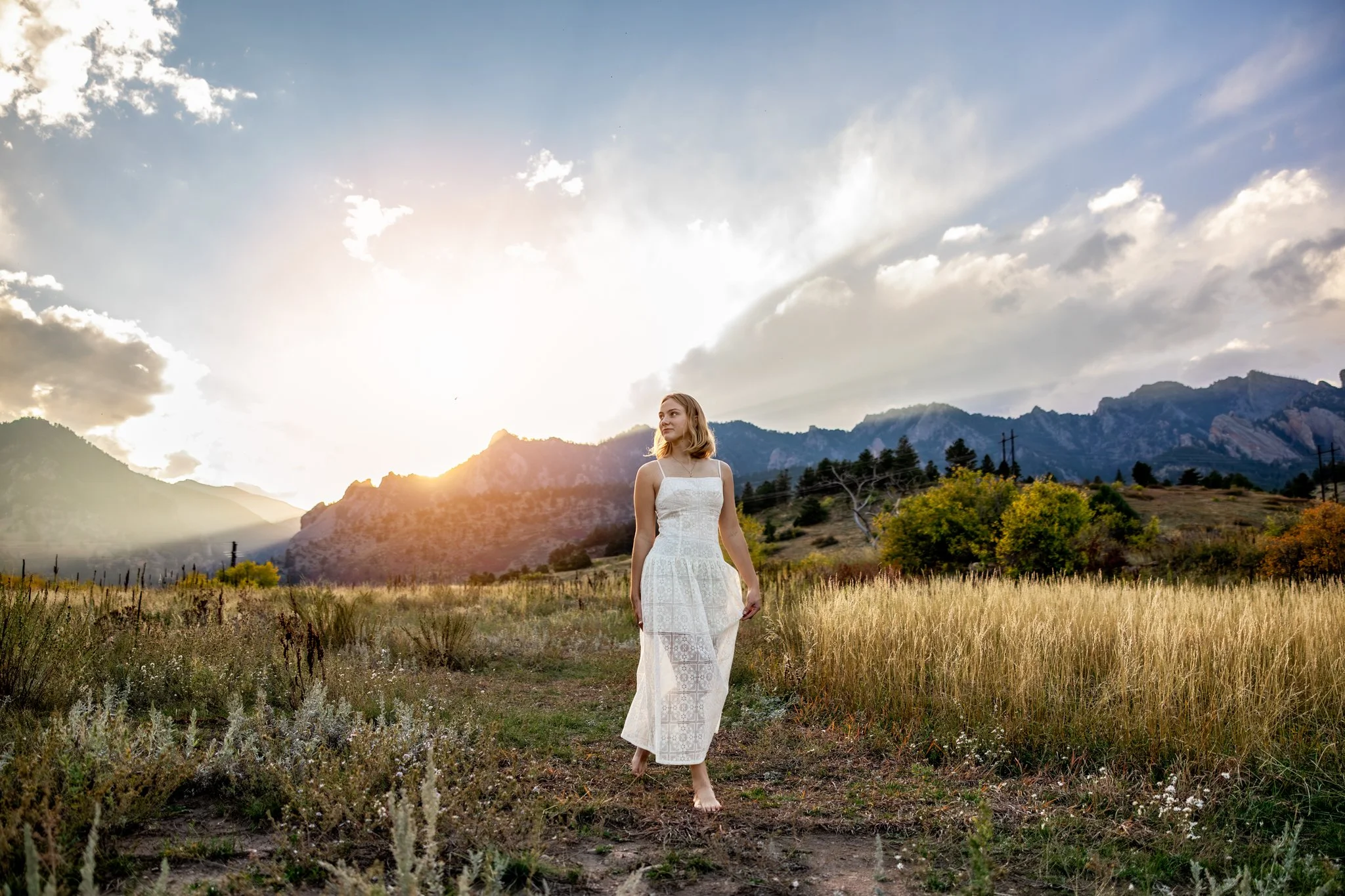 Boulder Colorado Photographer takes photograph of high school senior girl walking through open field with flatirons behind her at sunset.