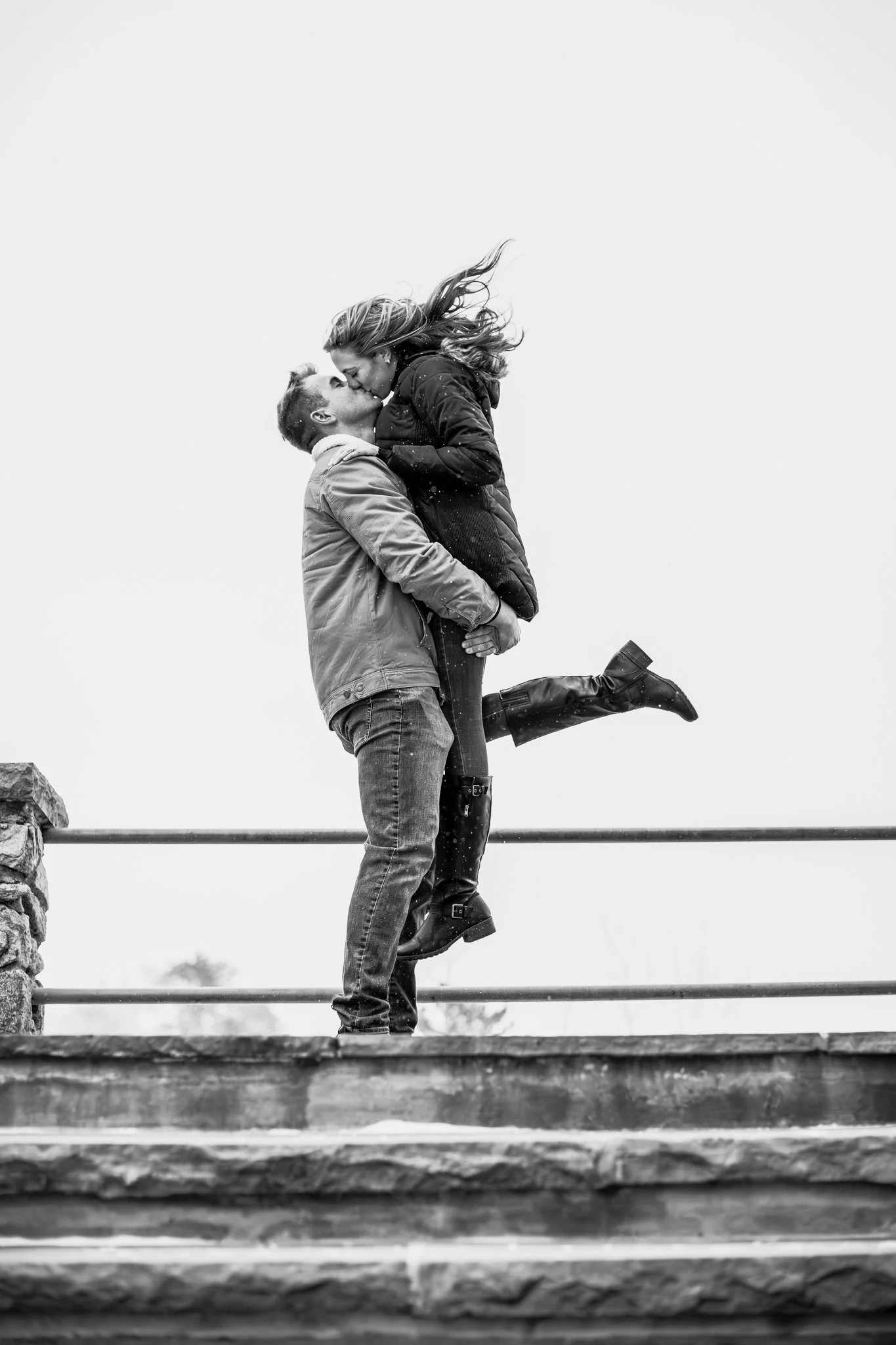 A couple kissing on a bridge, with the woman lifted in the man's arms, in black and white.