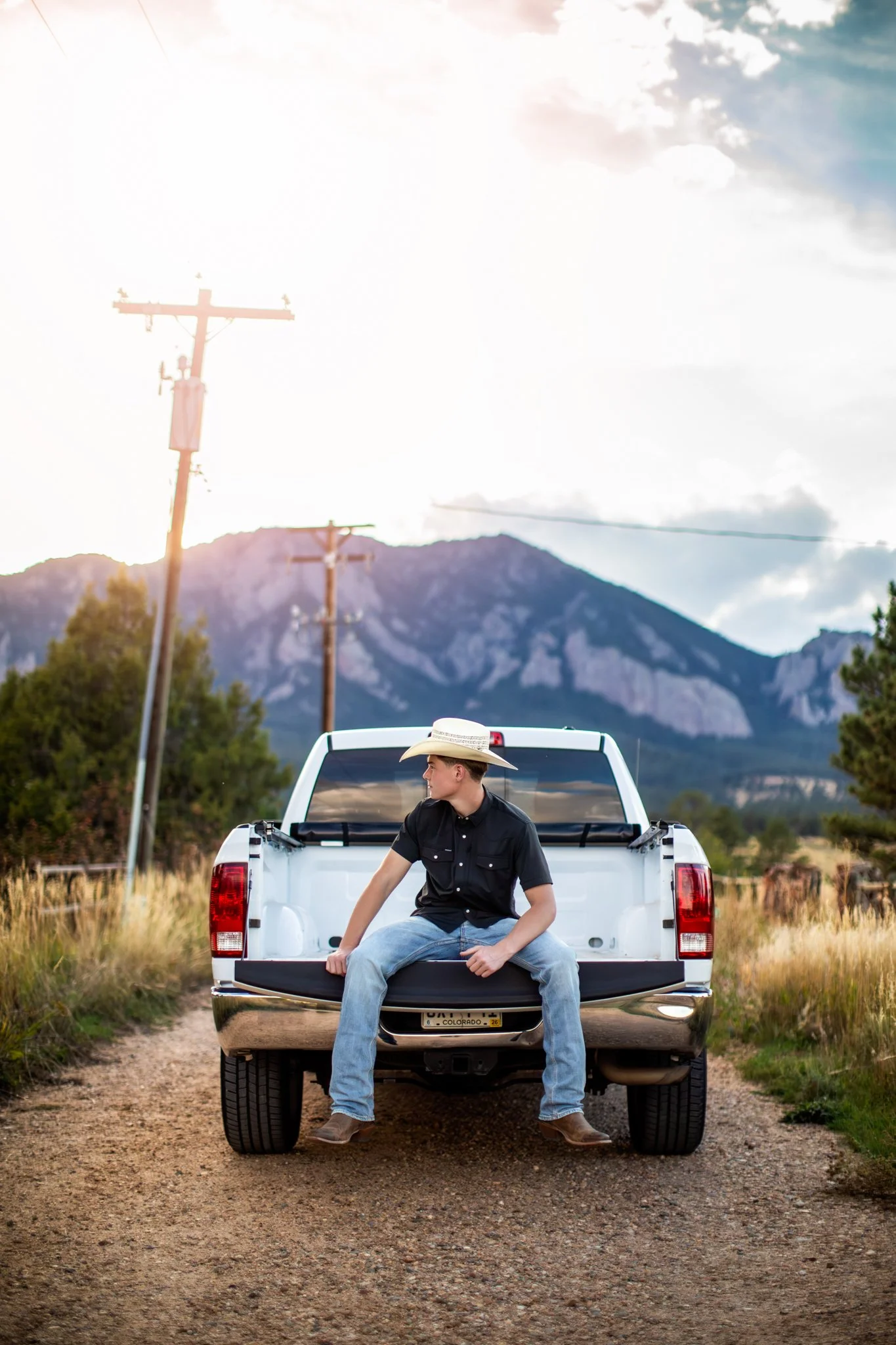 High School Senior Photographer captures picture of male high school student sitting the bed of his truck, wearing a cowboy hat at sunset.