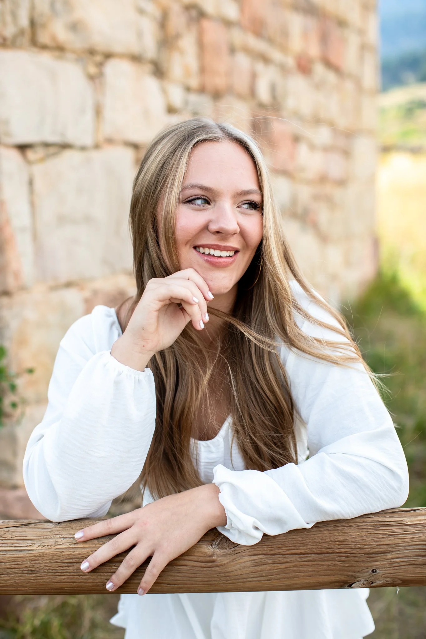 High school senior portraits of girl leaning on fence in long sleeved white dress.