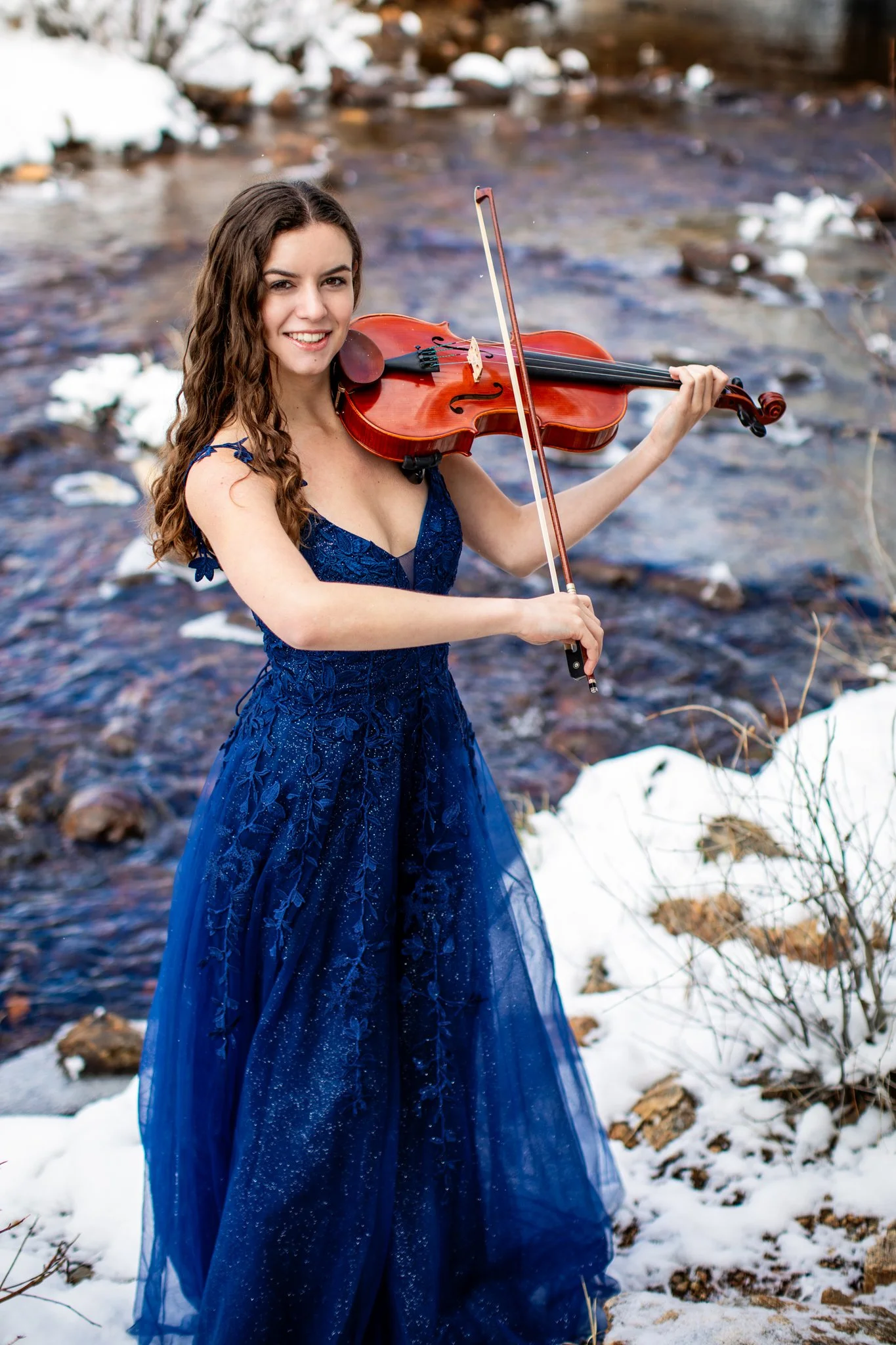Colorado Senior Photographer captures portrait of high school senior girl in Estes Park holding playing a violin by the river. 