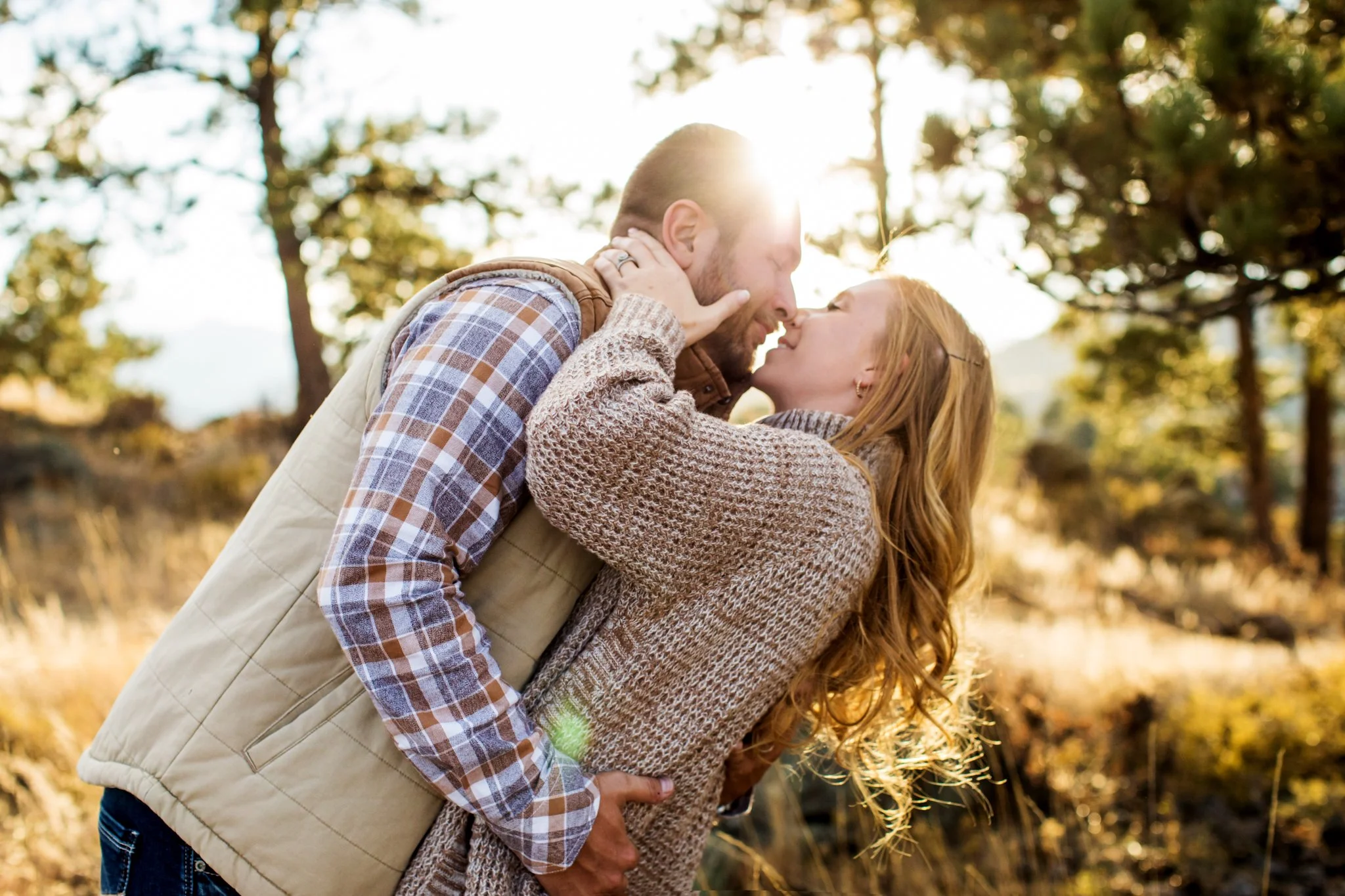 A couple sharing a romantic embrace outdoors with trees and sunlight in the background.