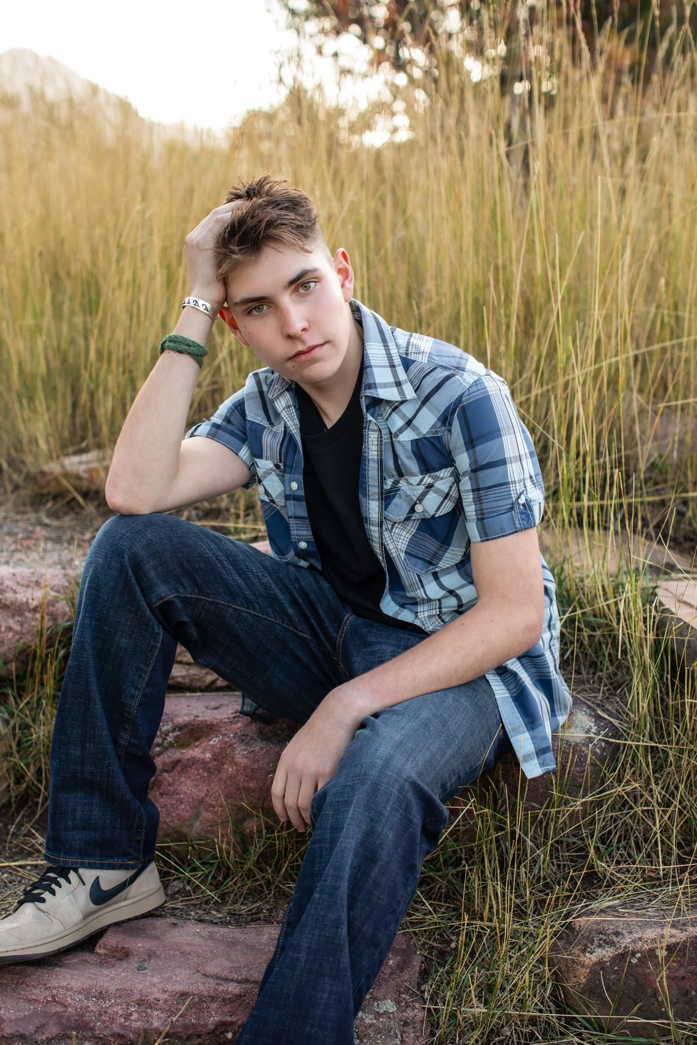 Photograph of a young man sitting on rocks and leaning his head into his hand.