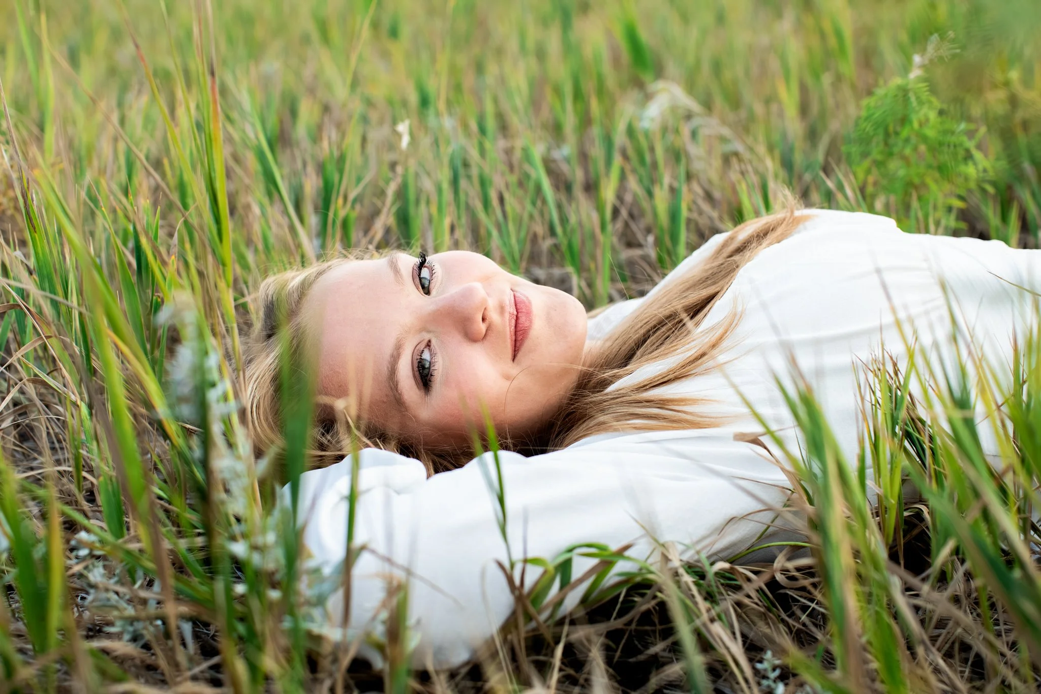 Boulder Senior Photographer captures image of senior girl laying down in green grass and looking at the camera.