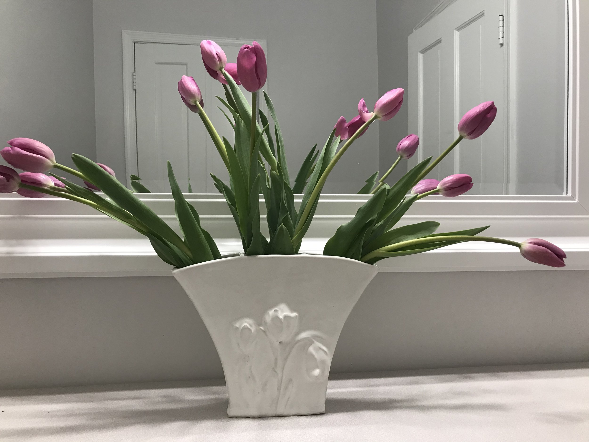 Handbuilt three-sectioned vase with a tulip motif, glazed white and holding fuchsia tulip flowers