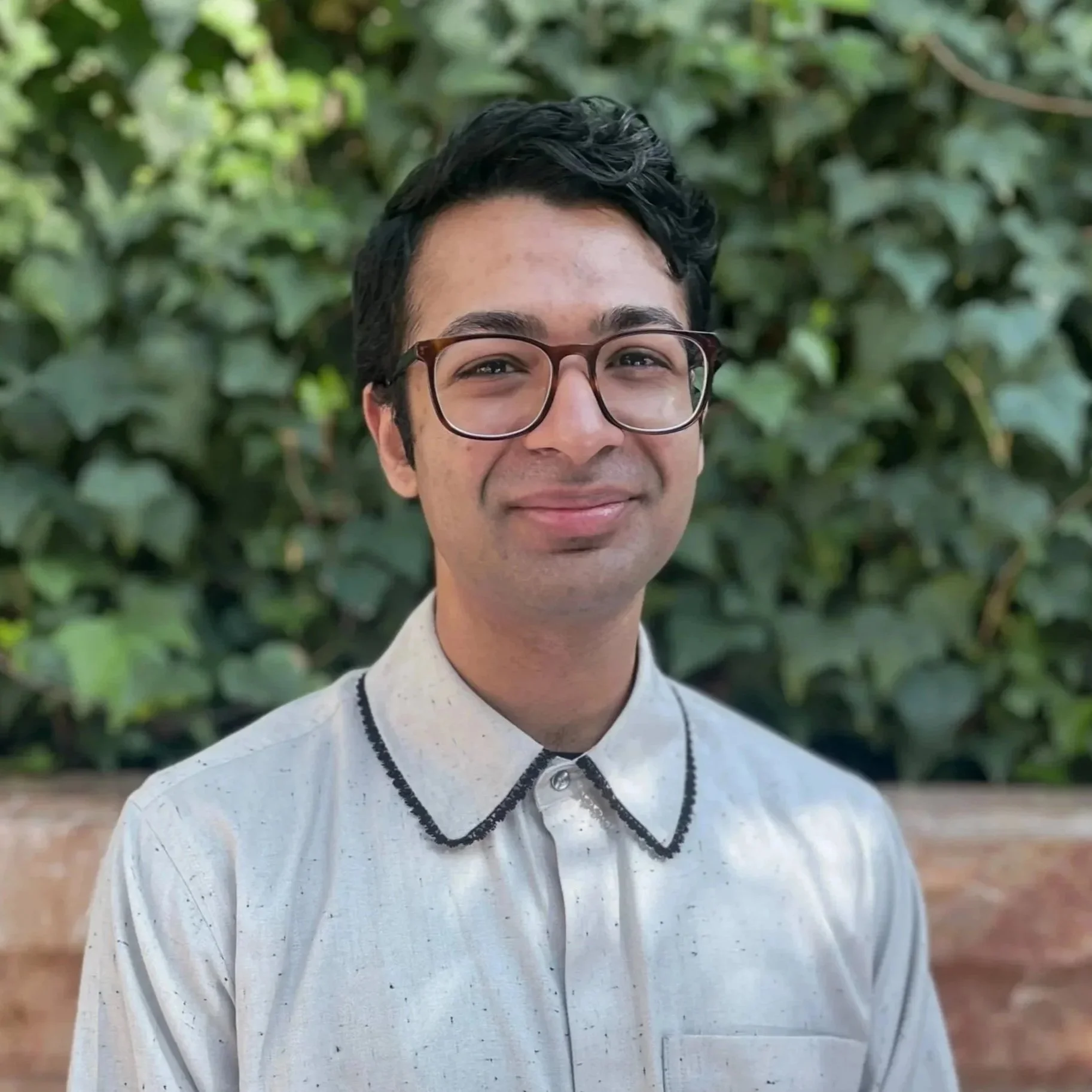 Smiling man wearing glasses and a cream button-down shirt with scalloped black trim around the collar.. 