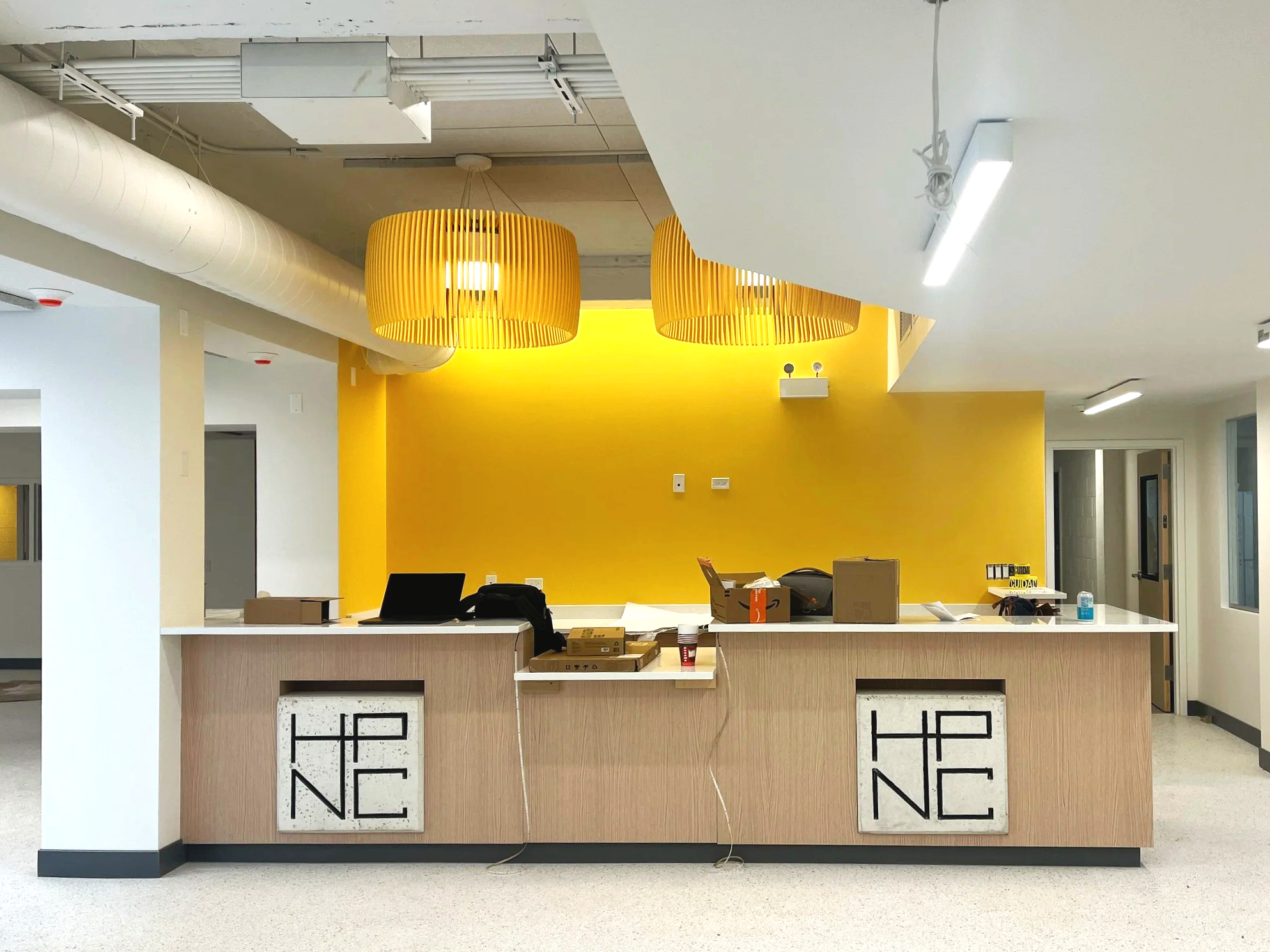 Empty reception desk in a modern office with a yellow accent wall and hanging yellow light fixtures.