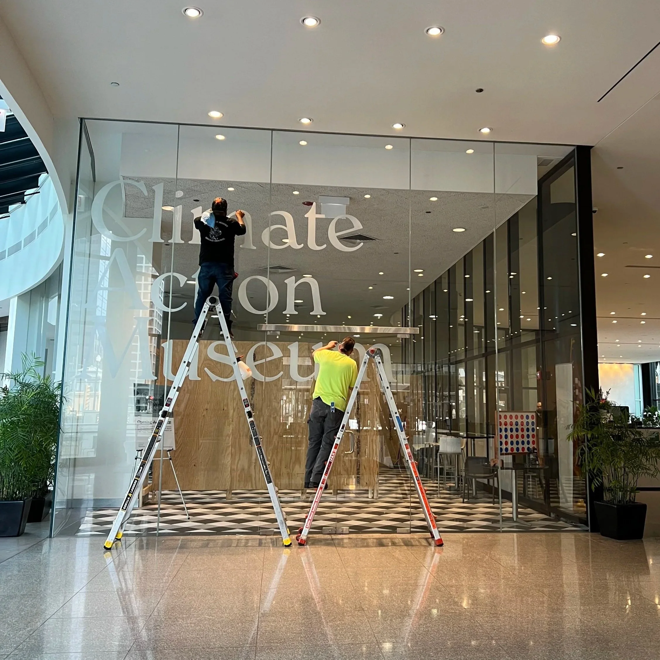 Installing translucent window text with a constructed exhibit wall visible in the background.