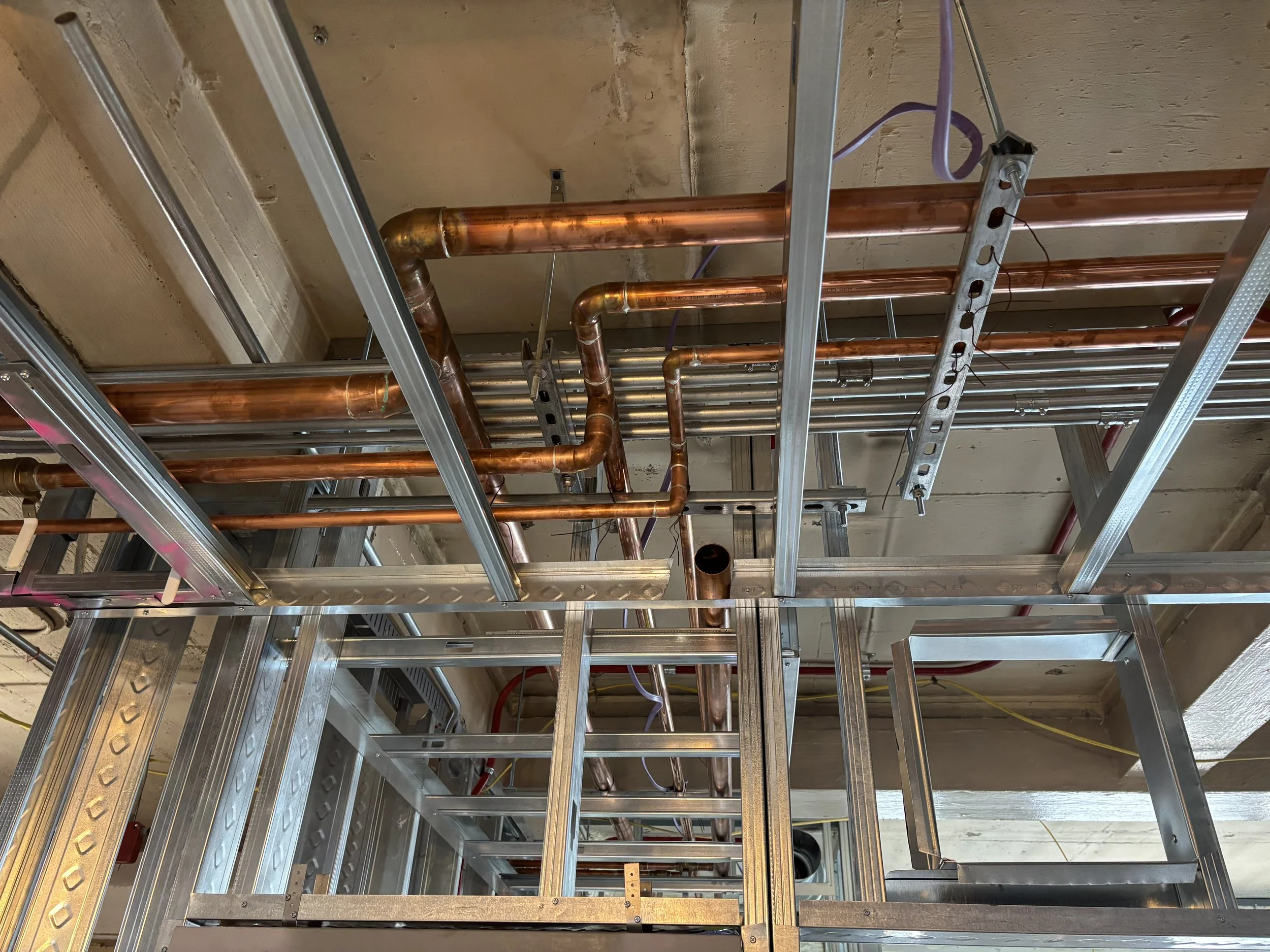 Construction site showing metal framing and copper pipes installed in the ceiling area.