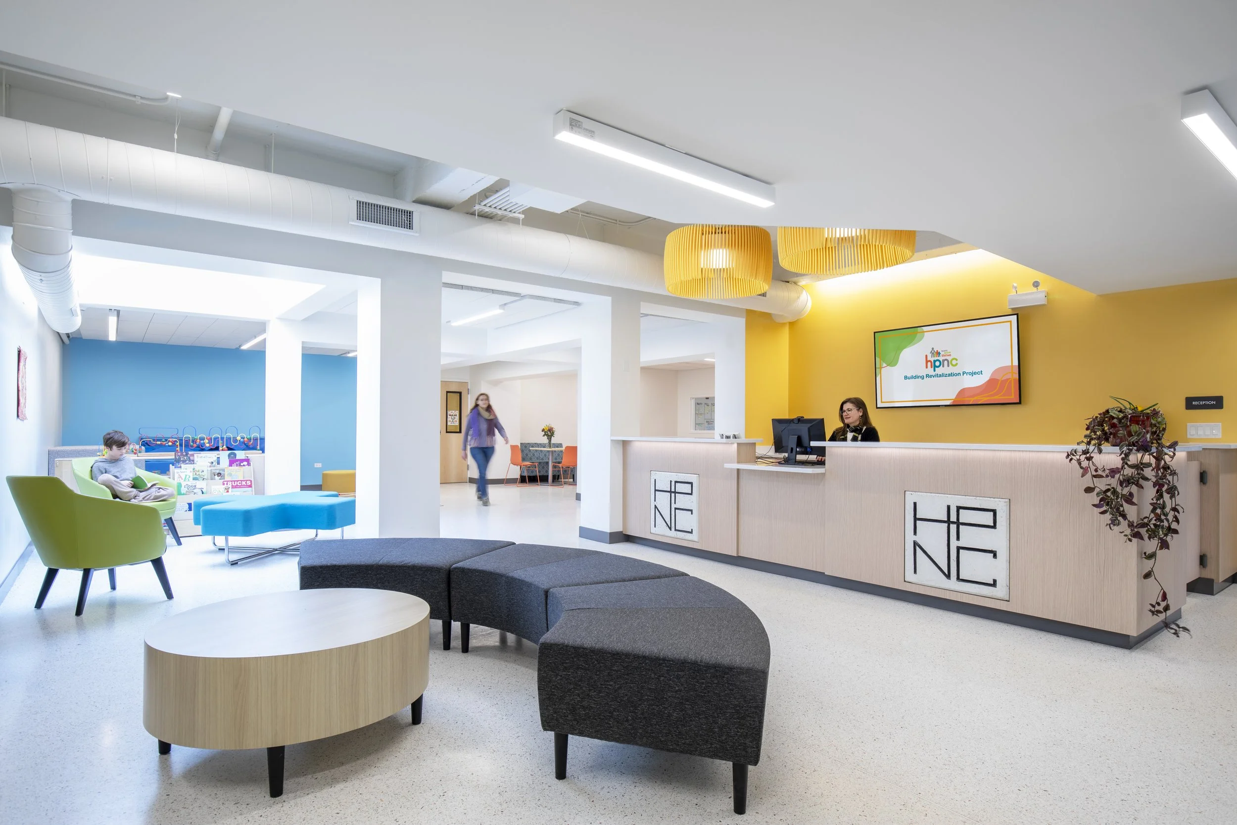 Empty reception desk in a modern office with a yellow accent wall and hanging yellow light fixtures.