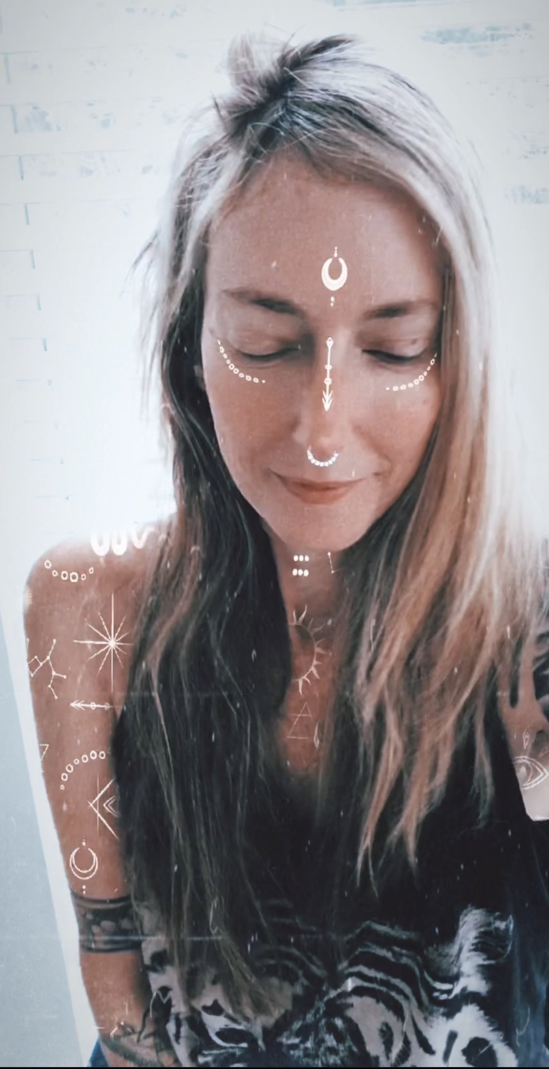 Young woman with long, wavy hair smiling with her eyes closed, decorated with celestial and geometric filter overlay.