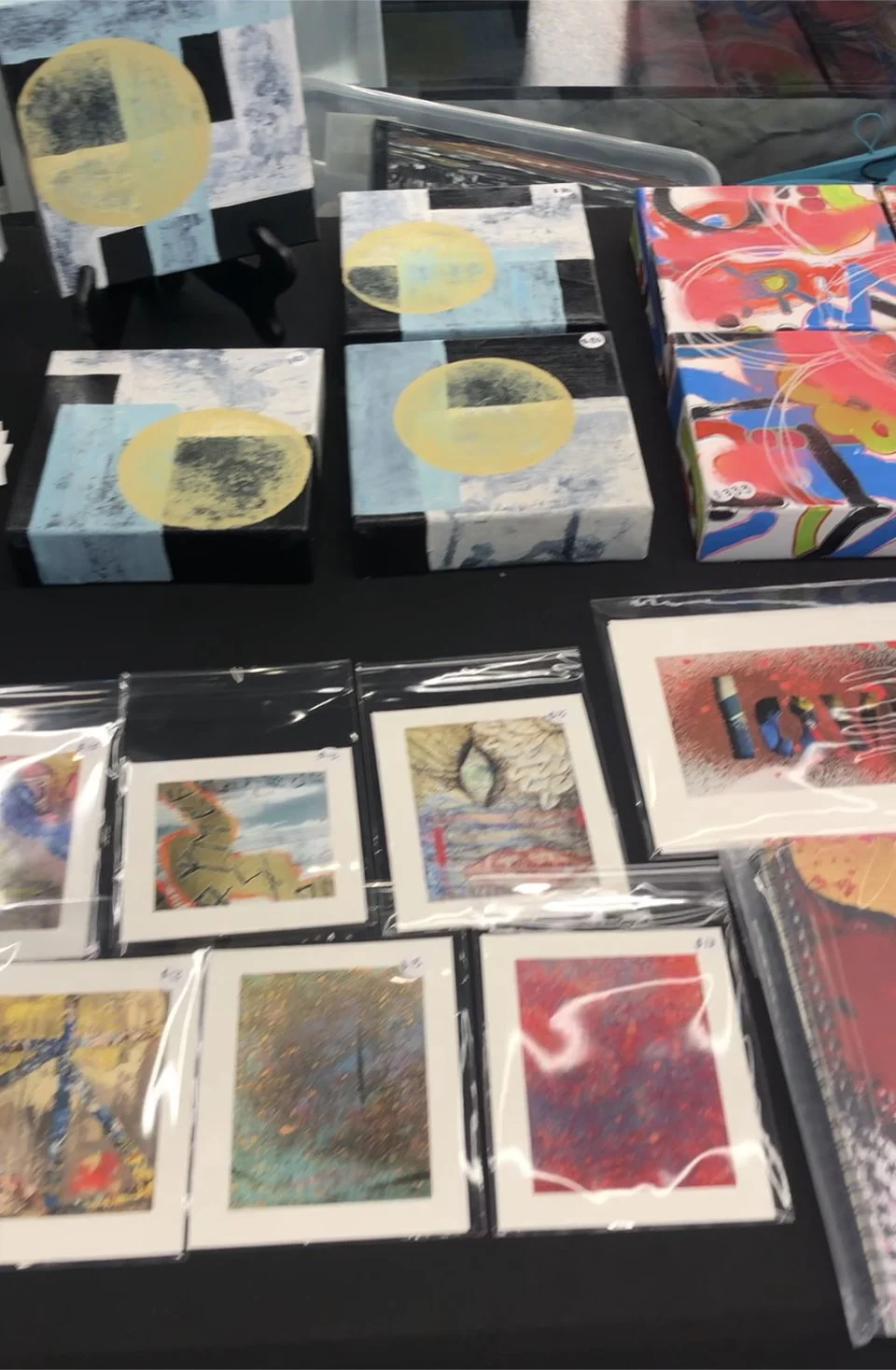 Assorted abstract art and paintings on display, including small framed pieces and wrapped artworks, some with colorful and textured designs.