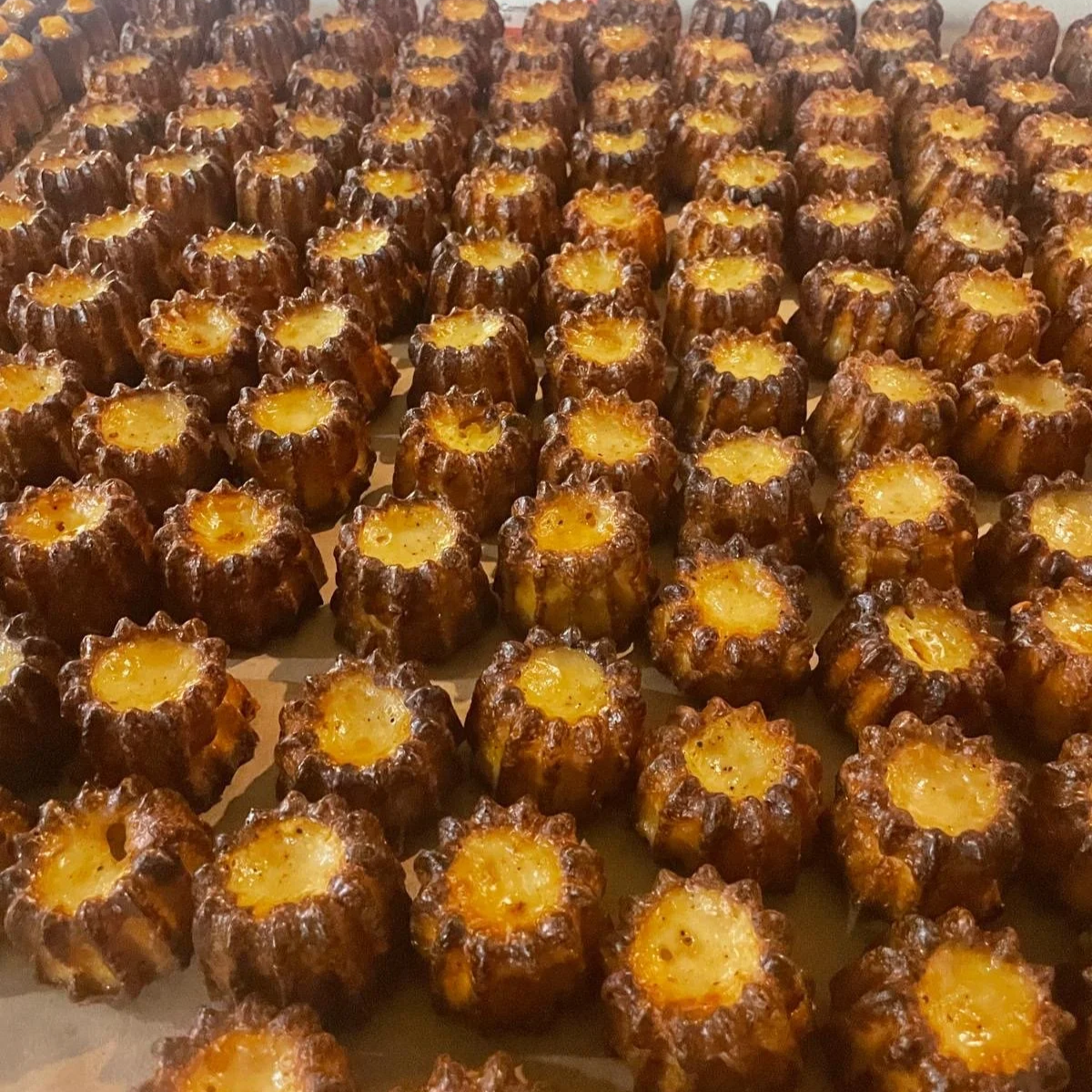 Multiple savoury canelés, a small French pastry with dark caramelized crust and soft-baked fondue-like interior, arranged on a tray.