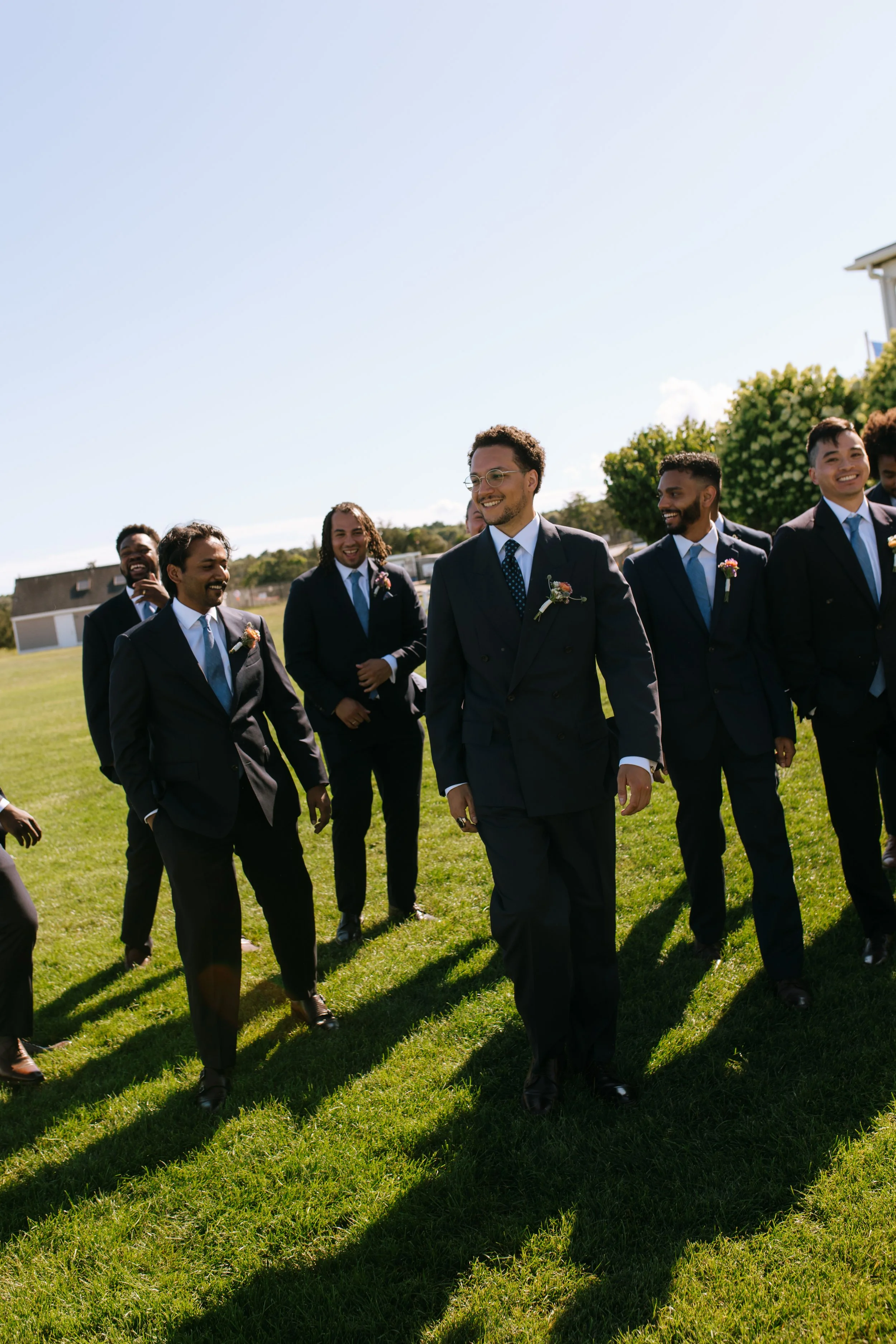 Group of men in suits walking on a grassy field, smiling and enjoying a sunny day.