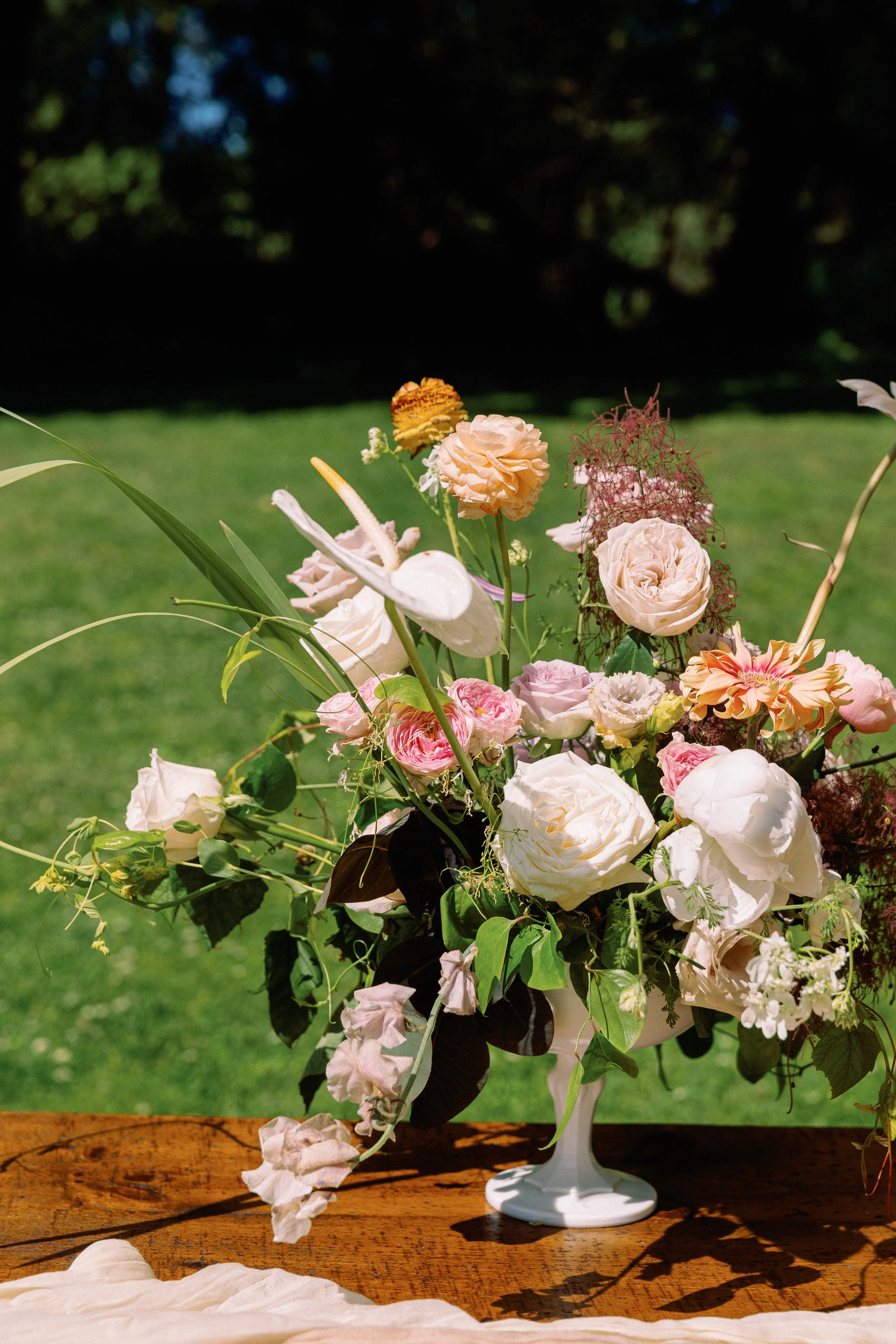 A colorful floral arrangement in a white vase on a wooden table outdoors.