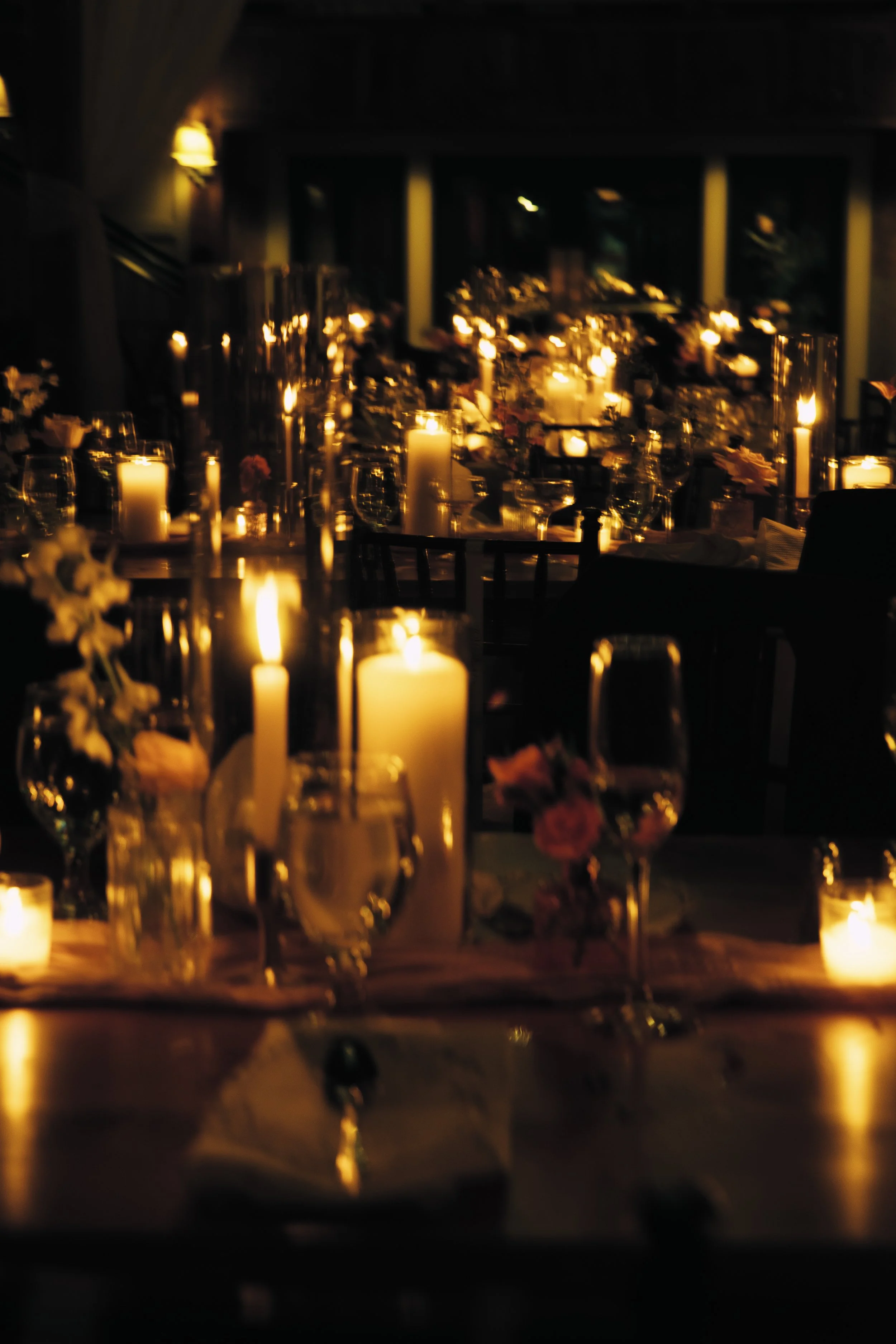 A dimly lit dinner event with candles on tables, decorated with flowers.