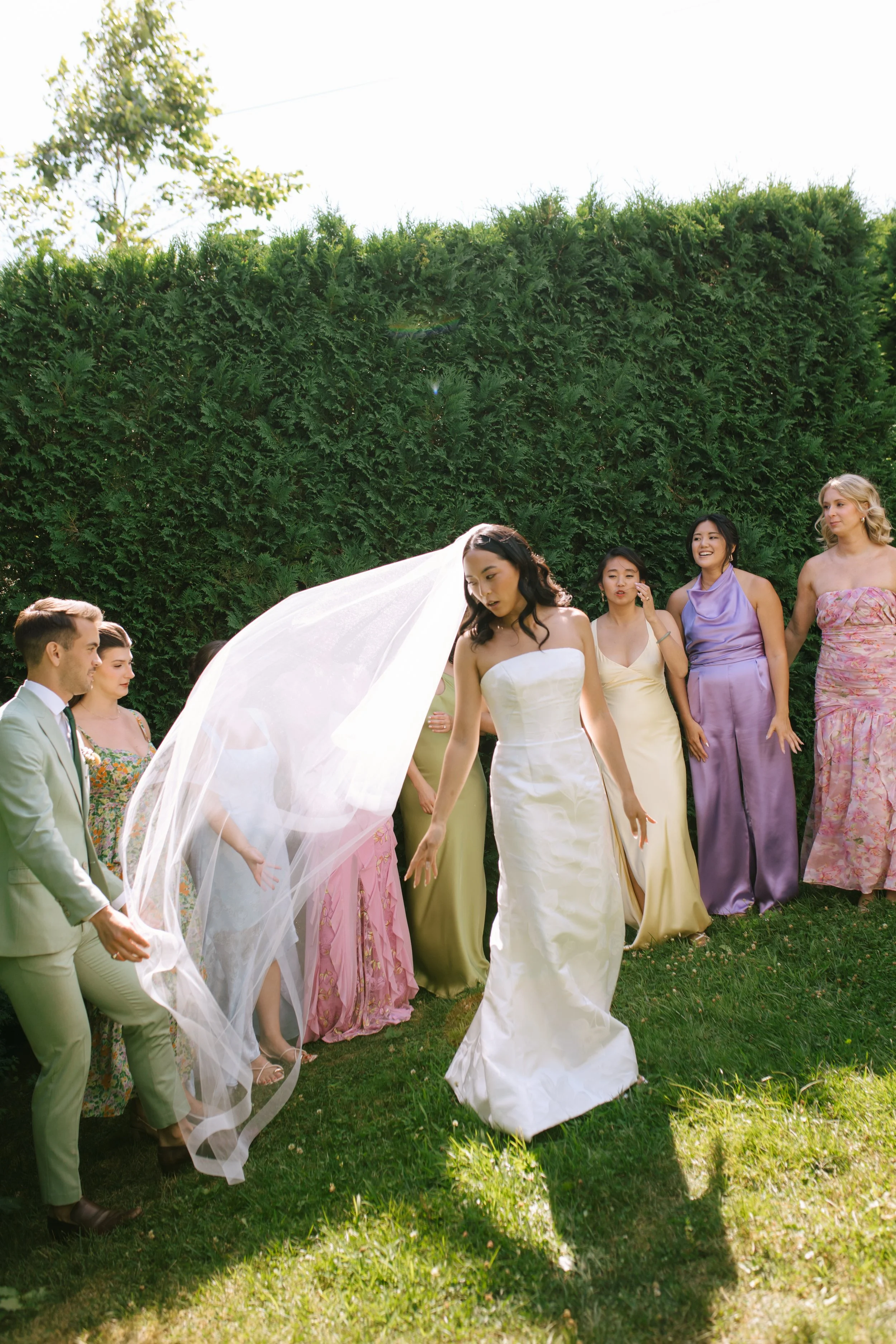 Bride in a white wedding dress with friends in colorful dresses outdoors.