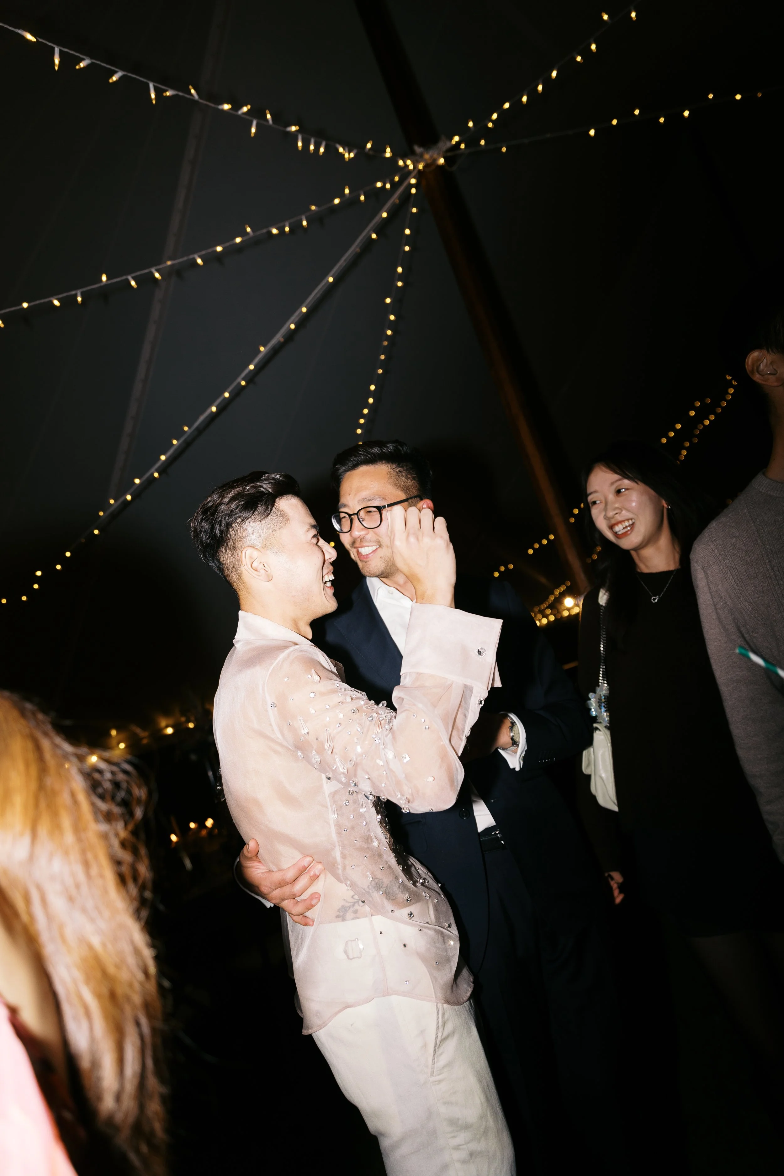 Group of people dancing and smiling under string lights at a celebration or party.