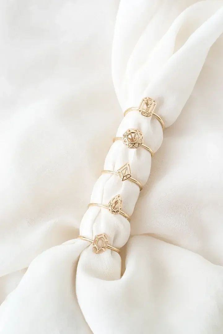 Five gold rings with geometric designs on a silky white fabric.