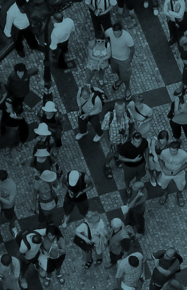 Overhead view of a crowd of people standing on a brick-paved street during the daytime.
