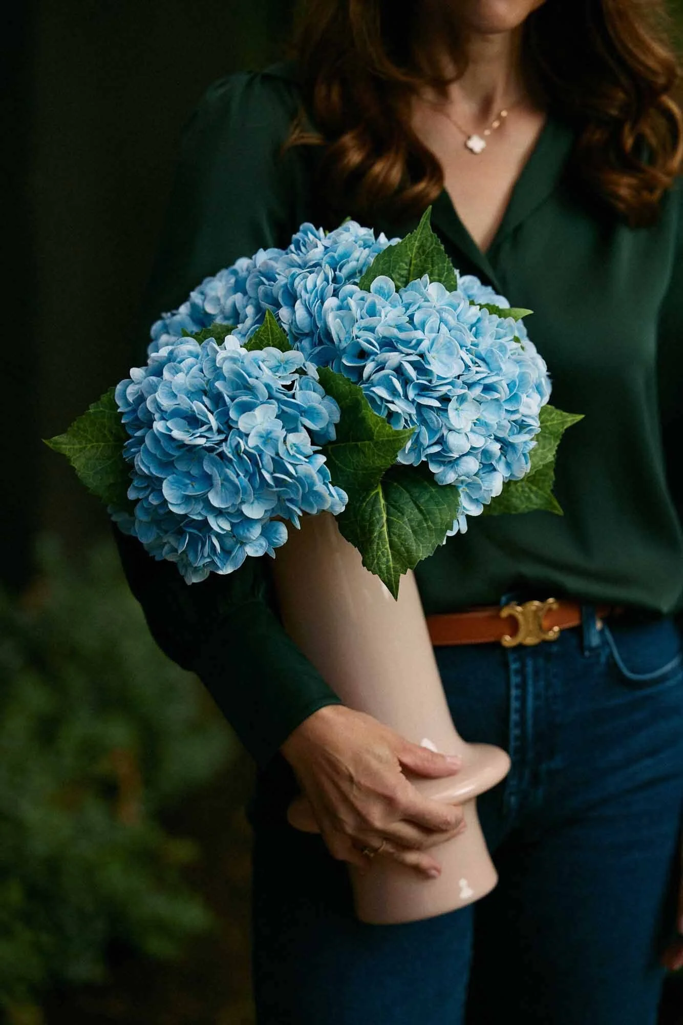 A woman holding a bouquet of blue hydrangea flowers while standing outdoors.