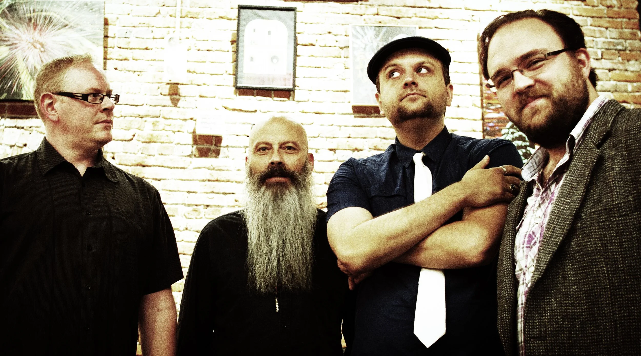 A group of six people standing on a grassy path with trees in the background, holding musical instruments and cases.