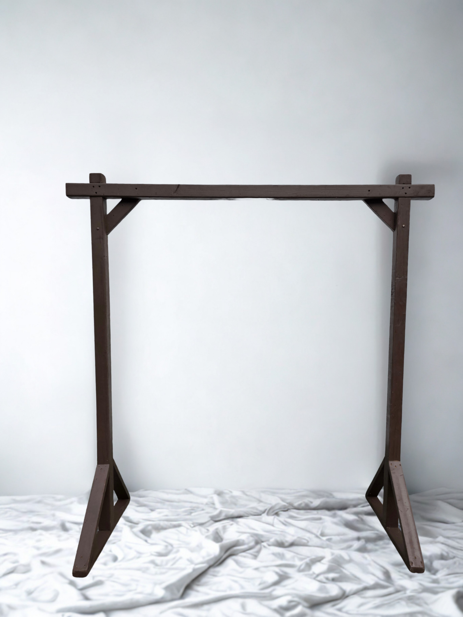 Wooden A-frame stand against a plain white wall, with a crumpled white fabric on the surface below.