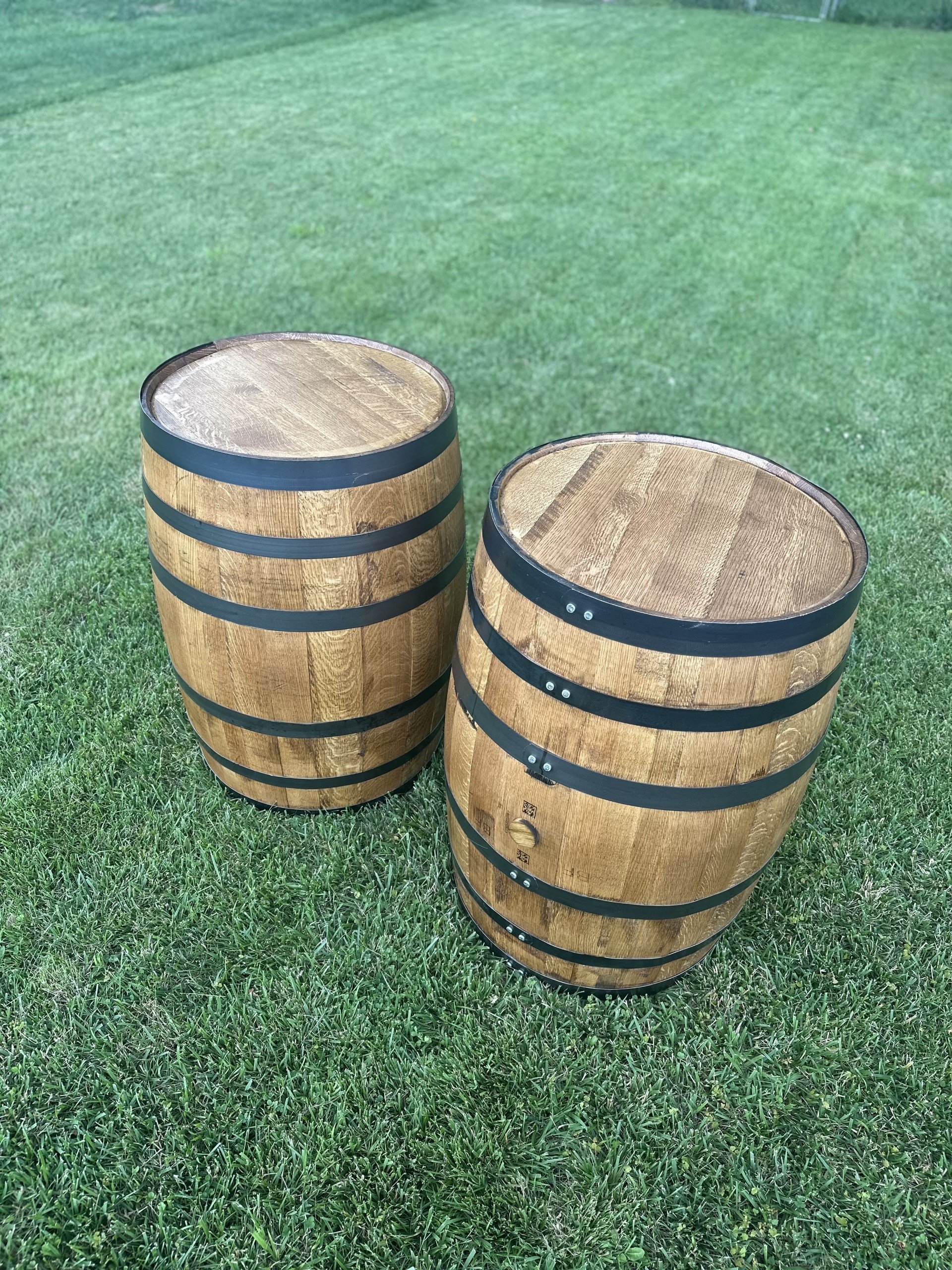 Two wooden barrels with metal bands placed on a grassy lawn.