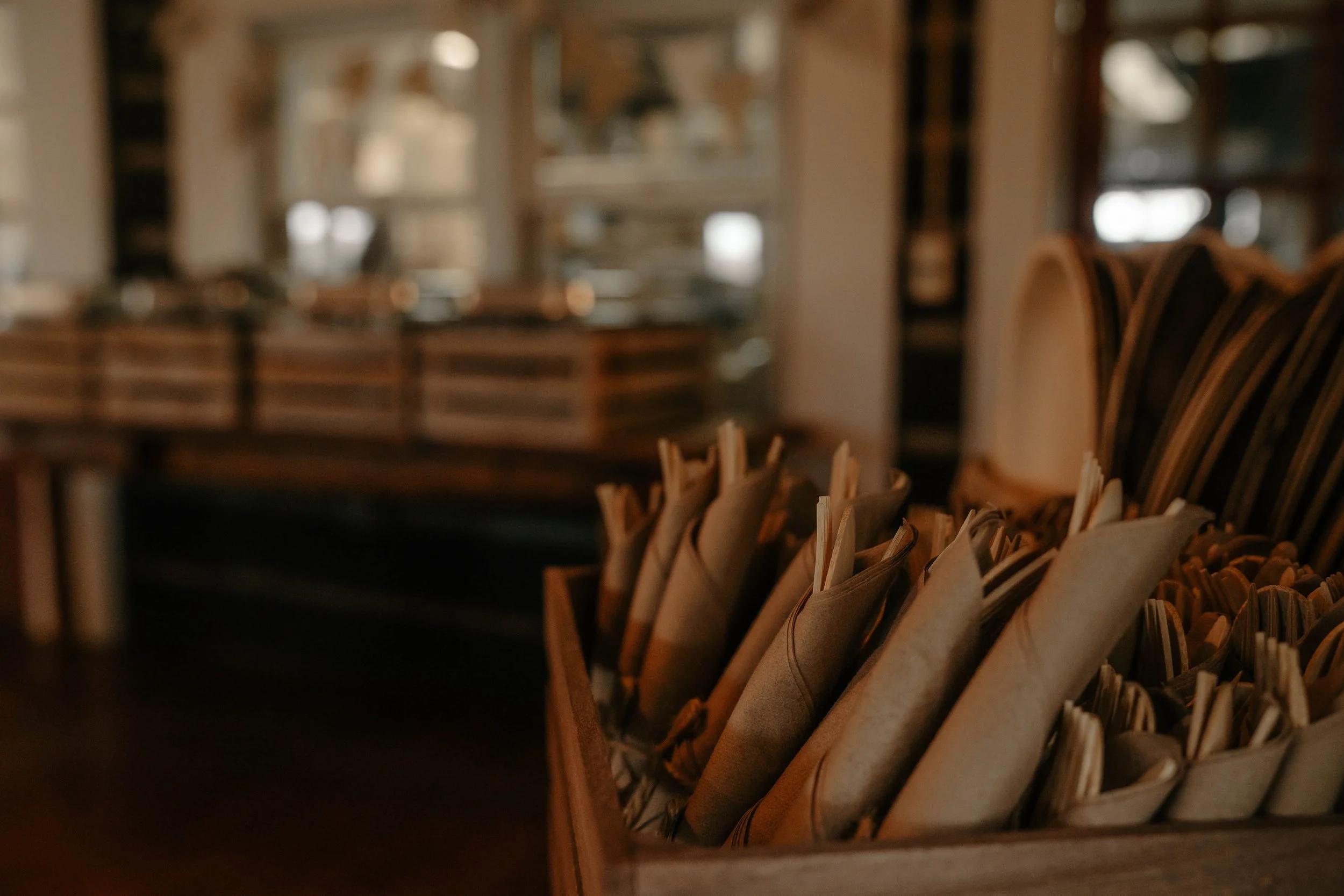 Close-up of a wooden tray filled with wrapped napkins or utensils in a restaurant setting with blurred background.