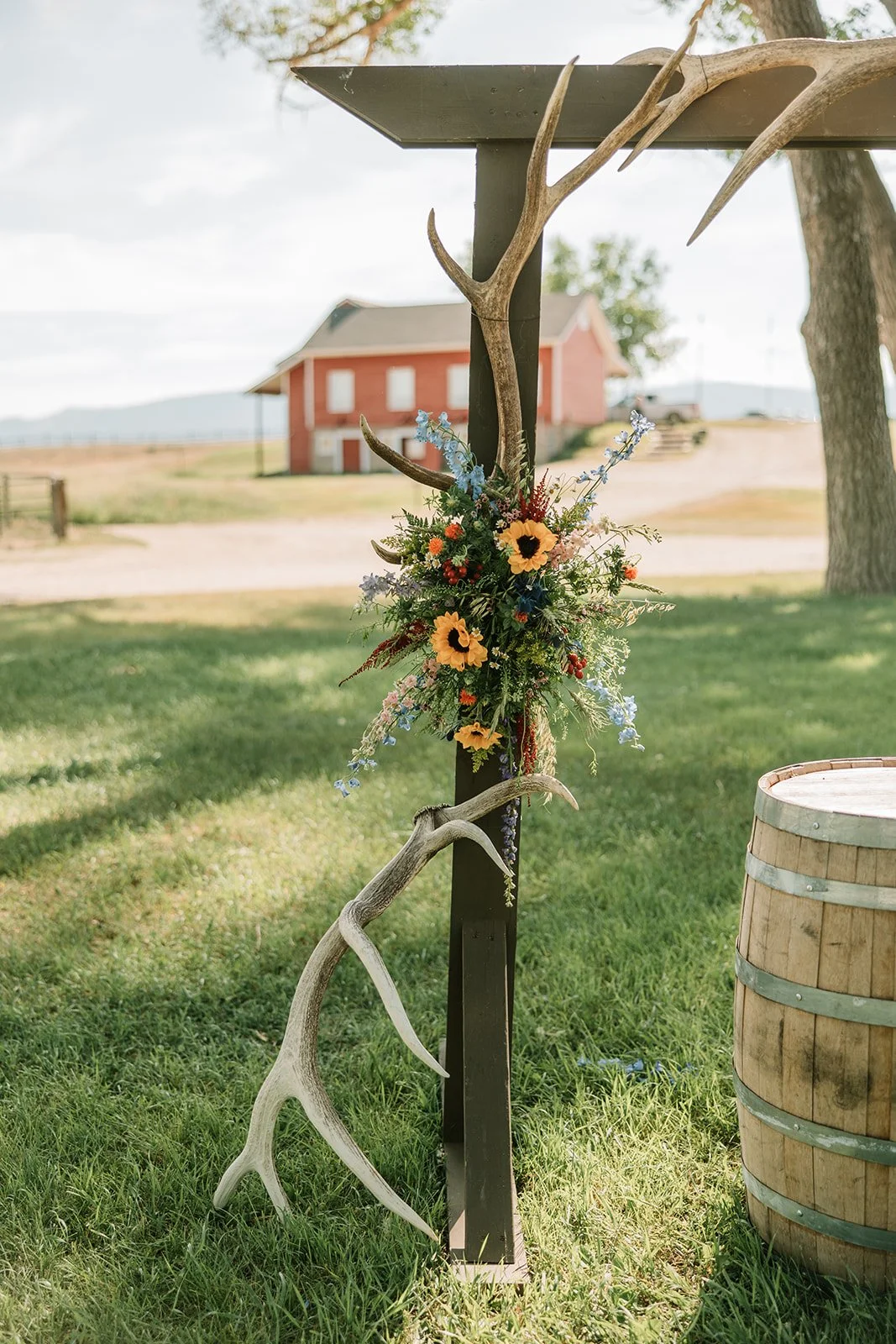 Decorative wooden barn star with antlers and a floral arrangement, outdoors on a sunny day with a red barn in the background.