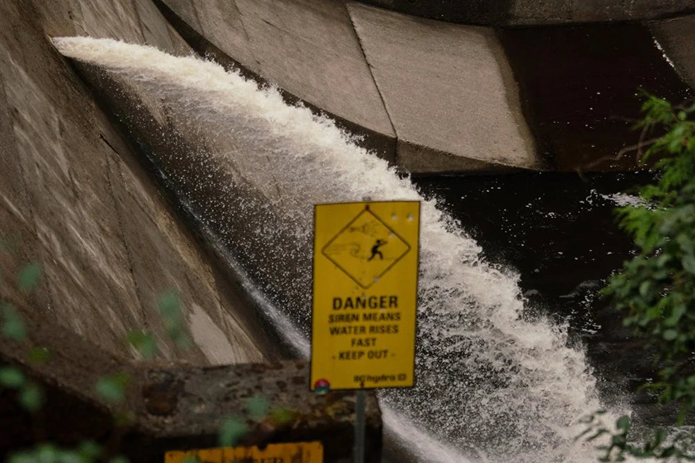 A single stream of water coming out from the concrete dam into the river below