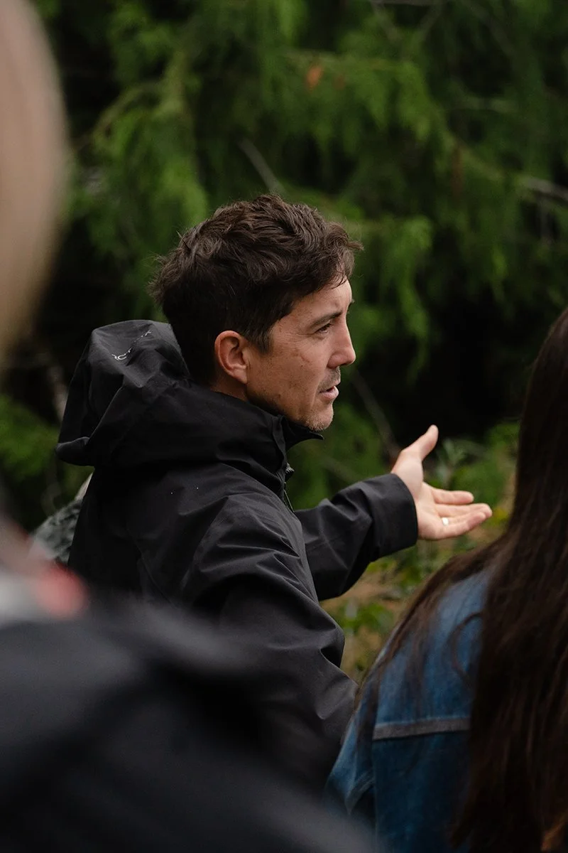 A close up through a crow of a man gesturing as he talks with trees in the background