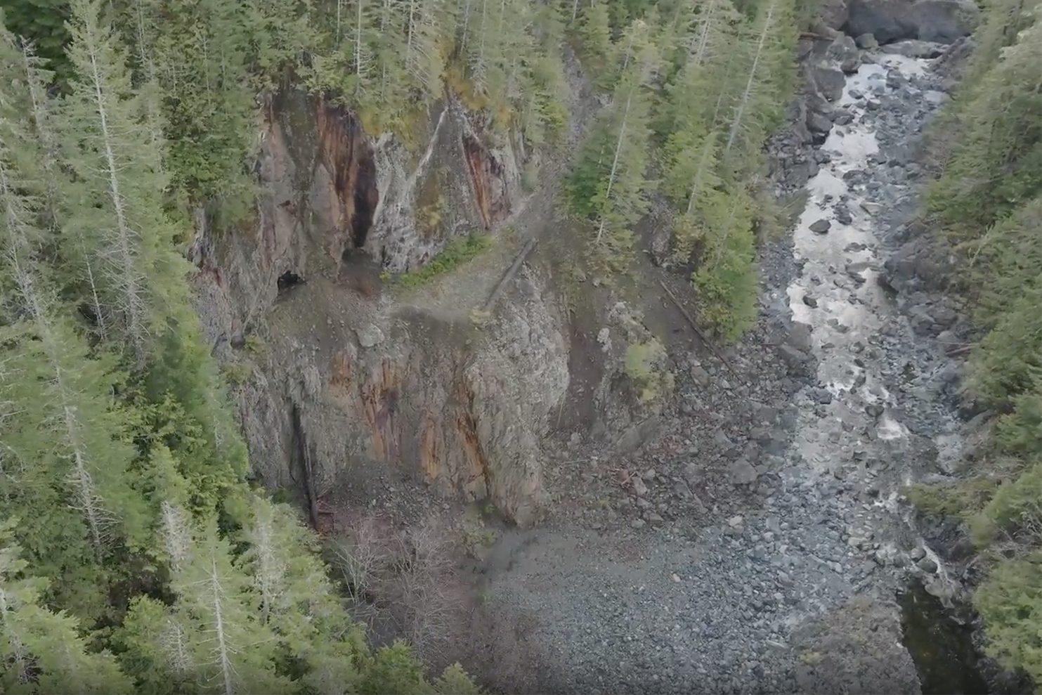 Tree lined, rocky canyon with holes blown into the left side back for mining