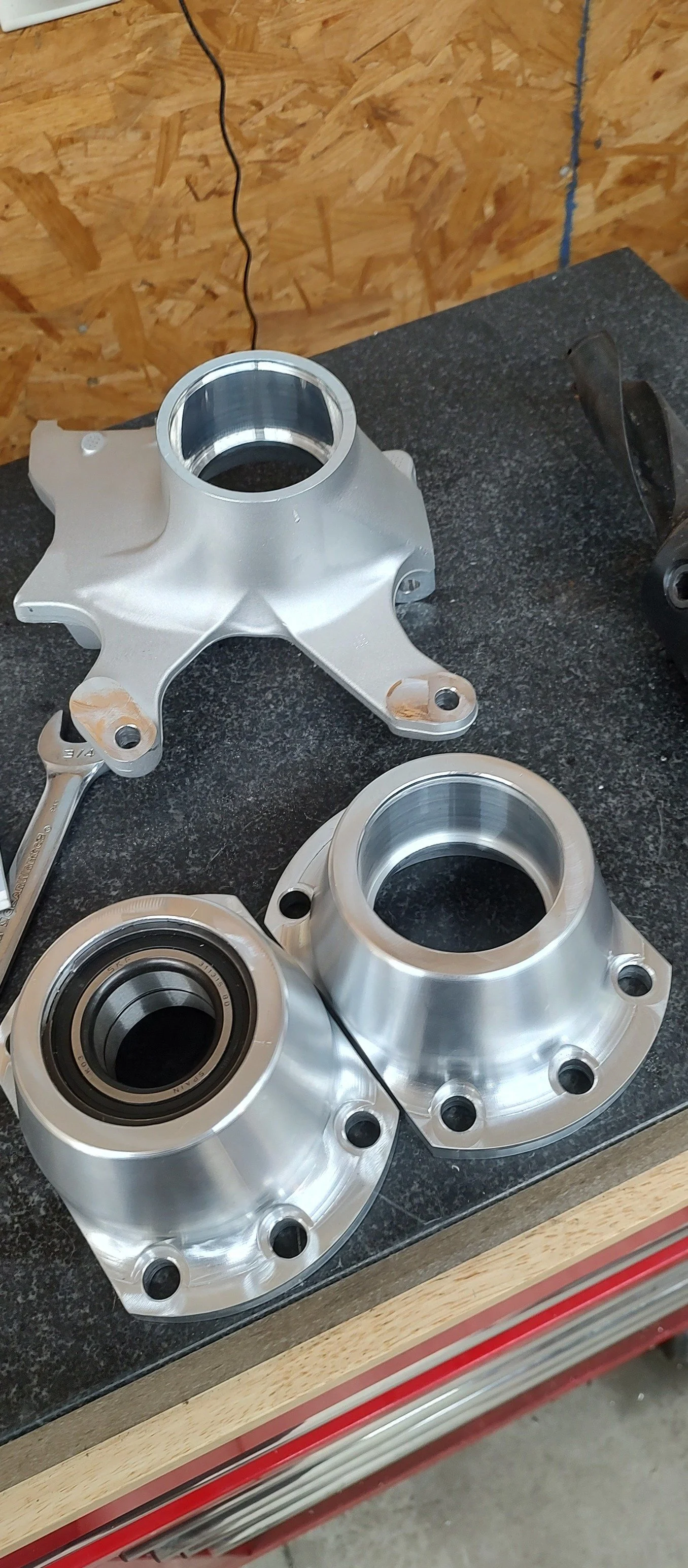 Three metallic motorcycle wheel hubs and a two-wrench on a black workbench in a workshop.