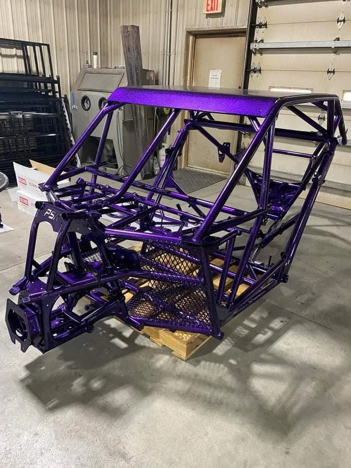 Purple painted metal racing car chassis on a wooden pallet in a workshop.