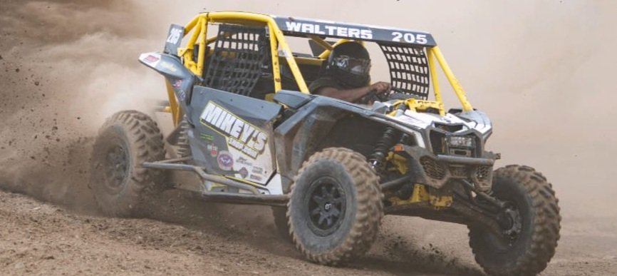 Off-road racing vehicle kicking up dust on dirt track.