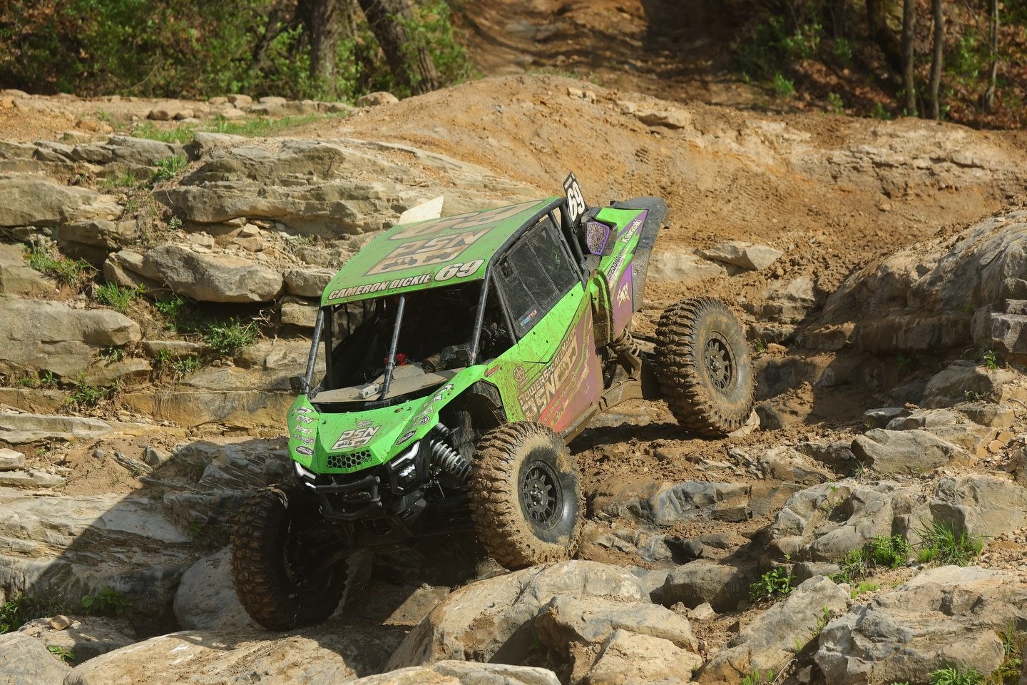 Green off-road UTV vehicle climbing over rocky terrain in a dirt and rocky outdoor landscape.