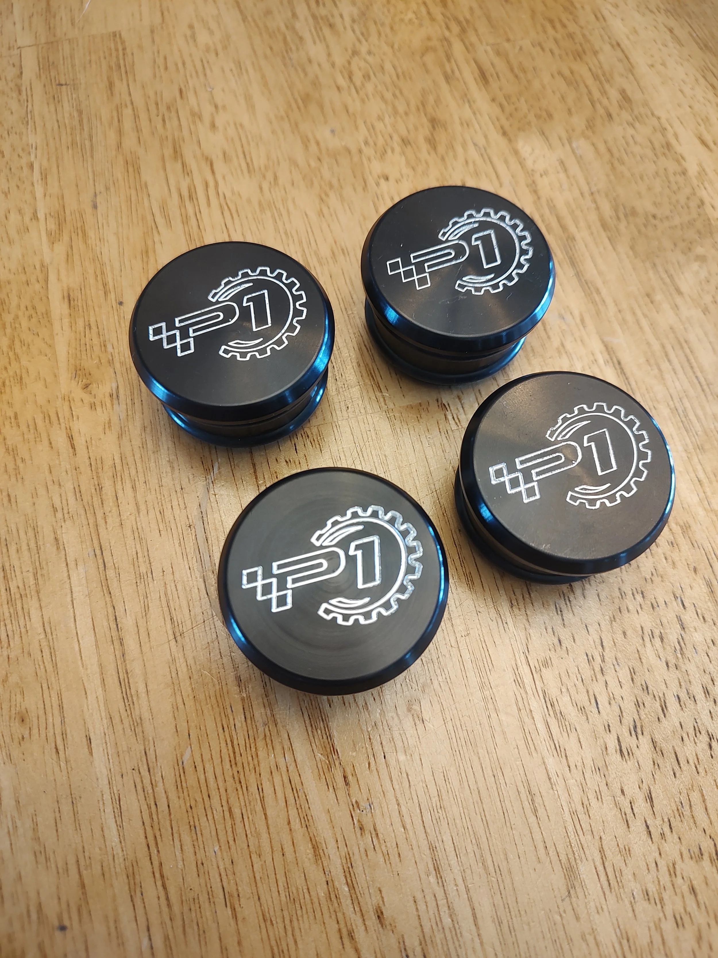 Multiple black containers with silver logos featuring a gear and the number 1, arranged on a wooden surface.