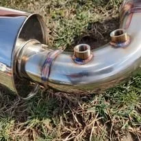 A metallic exhaust pipe with two smaller pipes attached, lying on grass.